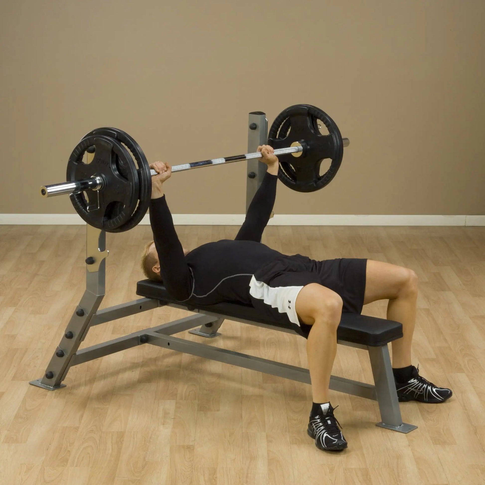 A person performing a bench press exercise on a Body-Solid Pro Clubline Flat Bench SFB125, lifting a barbell with weights in a gym setting.