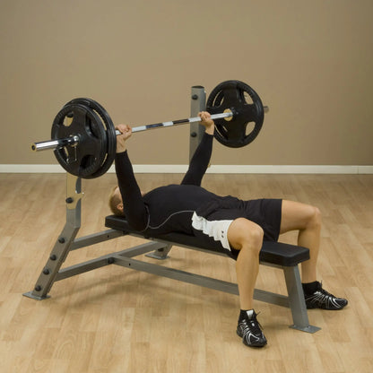 A person performing a bench press exercise on a Body-Solid Pro Clubline Flat Bench SFB125, lifting a barbell with weights in a gym setting.