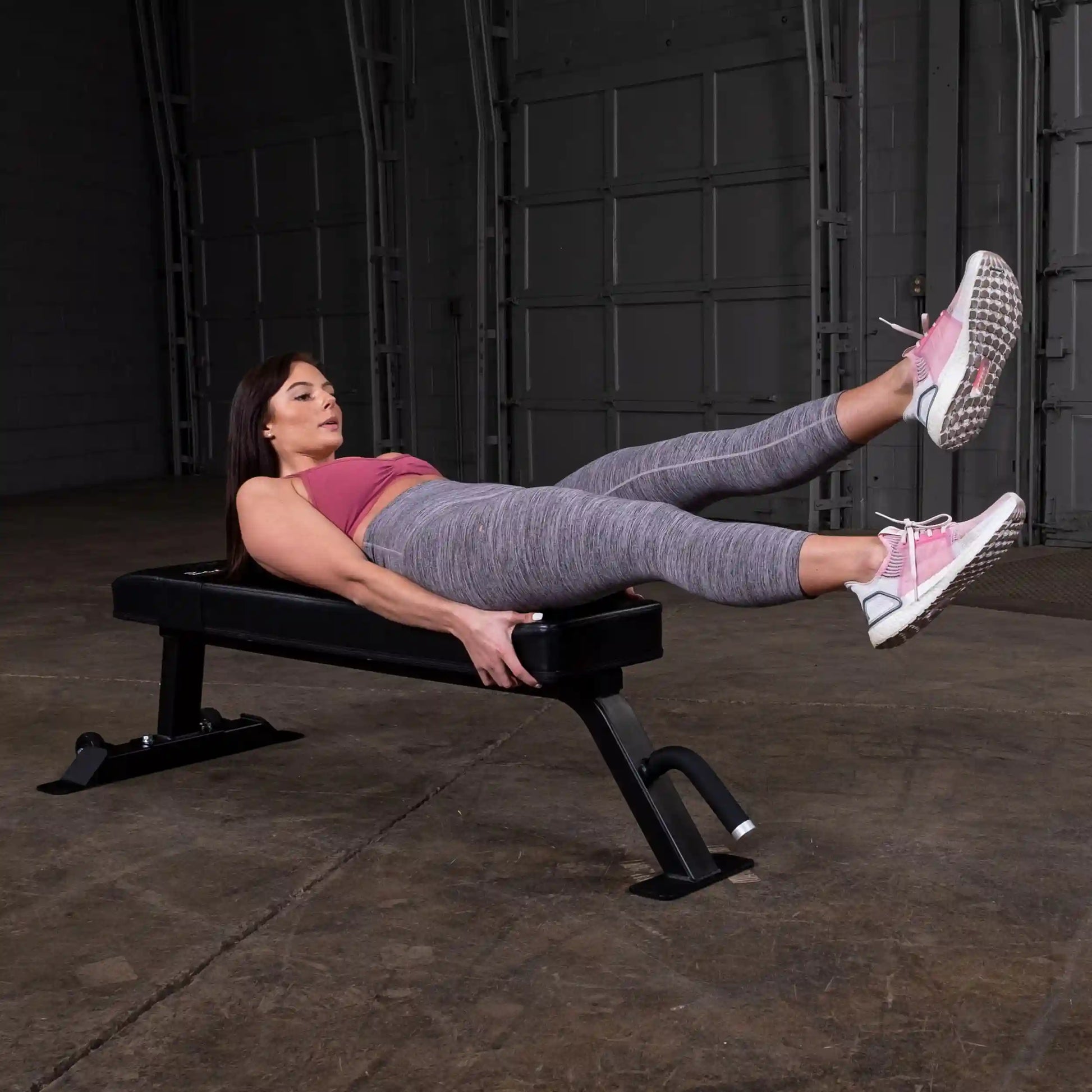 A person performing an exercise on the Body-Solid Pro Clubline Flat Bench SFB125, lying on their back with legs elevated, in a gym setting.