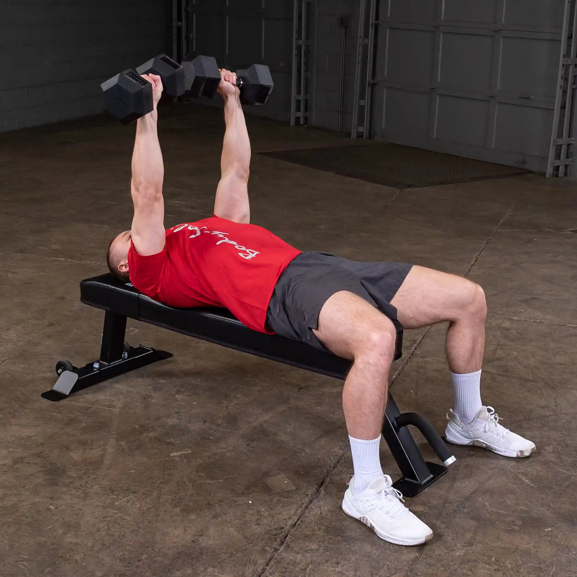 A person performing a dumbbell bench press on the Body-Solid Pro Clubline Flat Bench SFB125 in a gym setting.