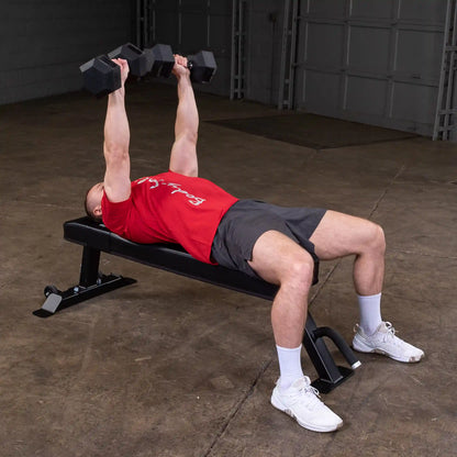 A person performing a dumbbell bench press on the Body-Solid Pro Clubline Flat Bench SFB125 in a gym setting.