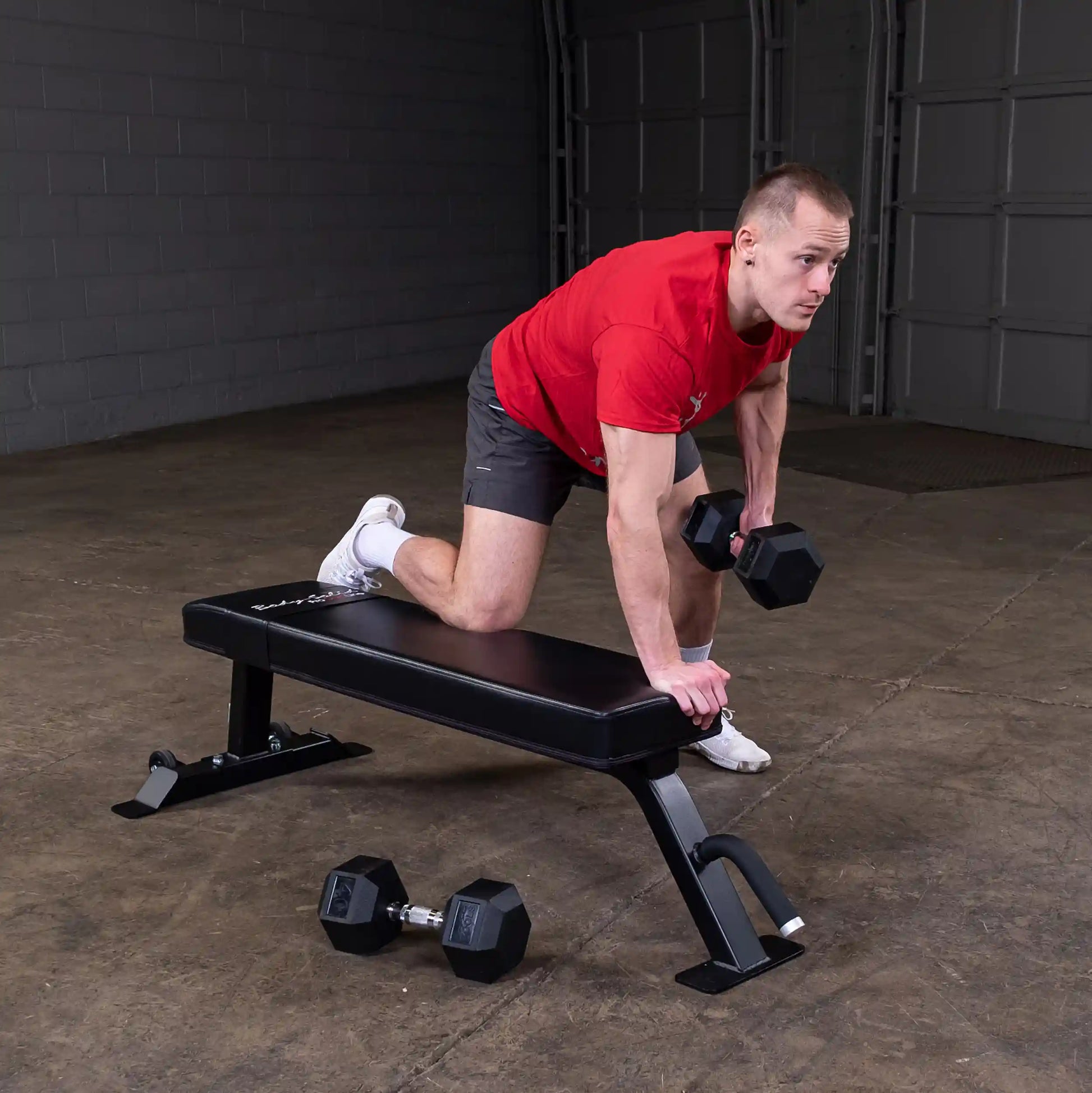 A man performing an exercise on the Body-Solid Pro Clubline Flat Bench SFB125, holding dumbbells, in a gym setting.