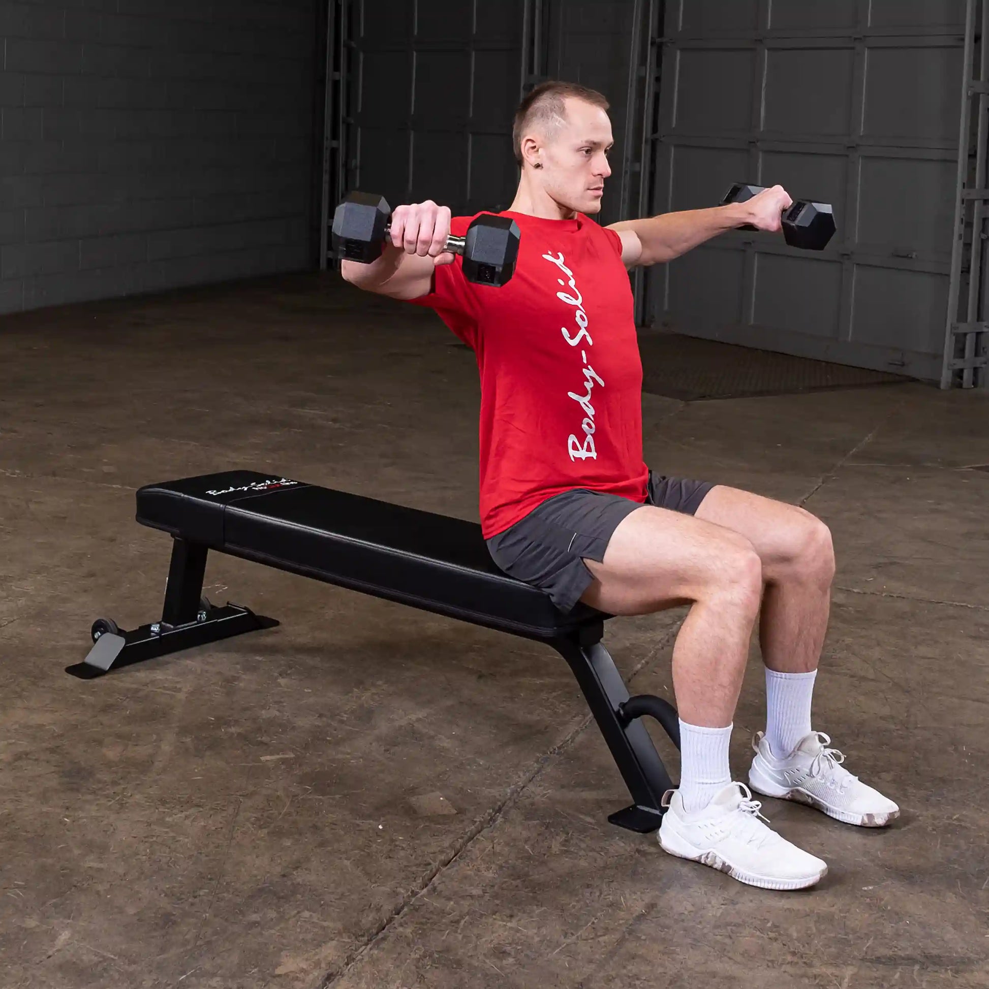 A man performing a dumbbell exercise while seated on the Body-Solid Pro Clubline Flat Bench SFB125 in a gym setting.