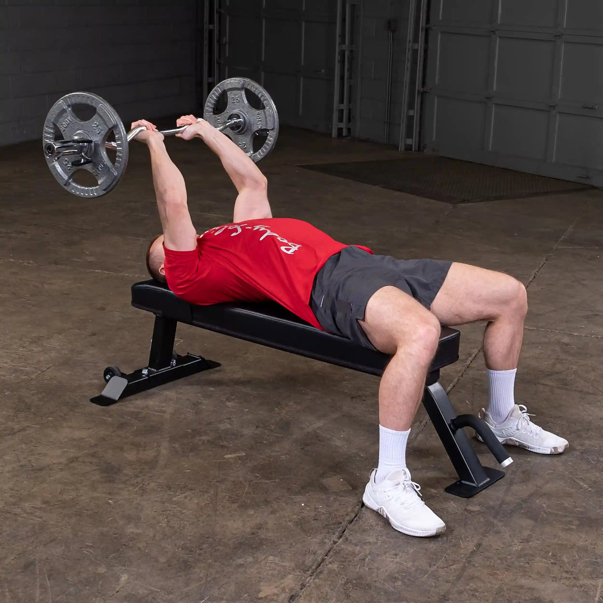 A person performing a bench press exercise on the Body-Solid Pro Clubline Flat Bench SFB125, lifting a barbell with weights in a gym setting.