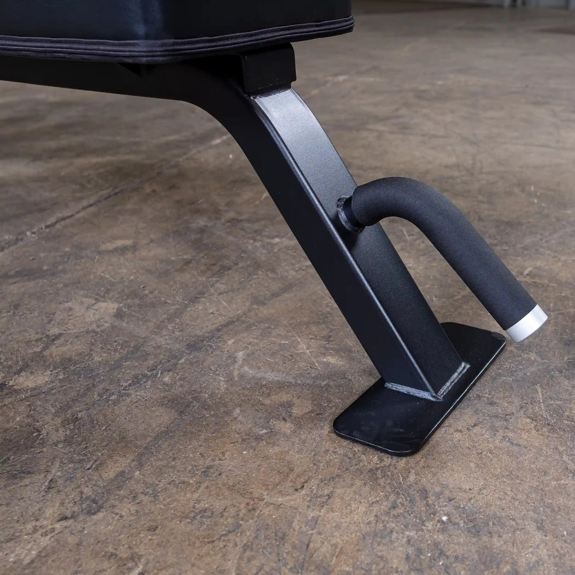 Close-up view of the leg of the Body-Solid Pro Clubline Flat Bench SFB125, showcasing its sturdy metal construction and rubber grip for stability on a textured floor.