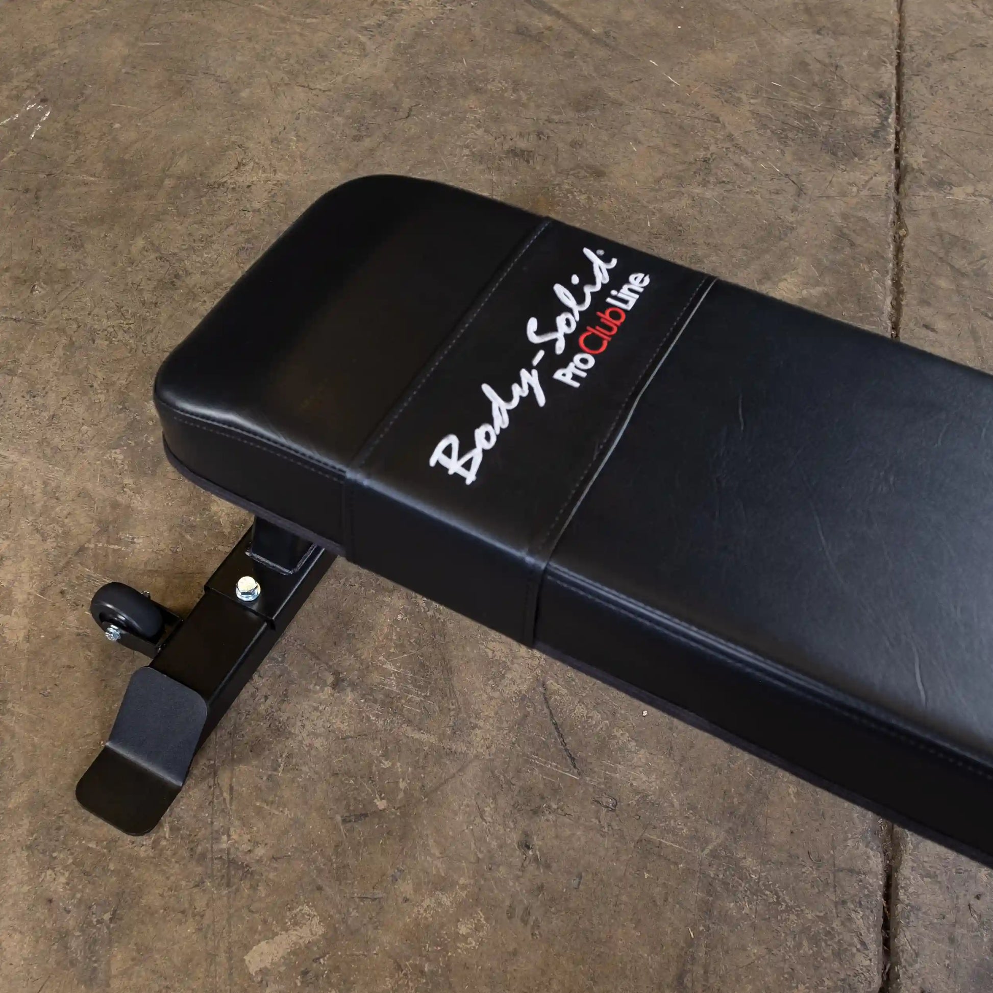 Close-up of the Body-Solid Pro Clubline Flat Bench SFB125, featuring a black padded surface and a sturdy base on a concrete floor.