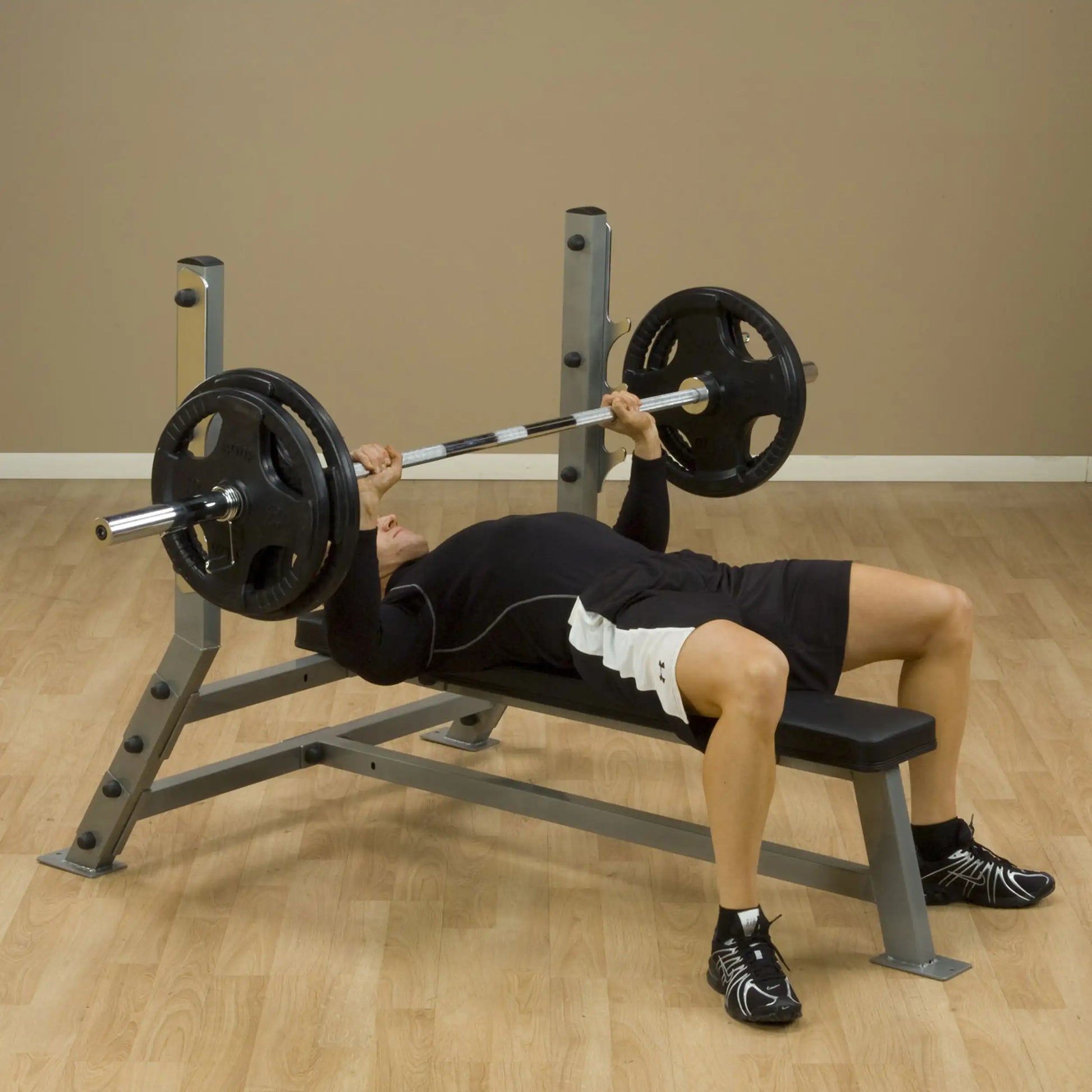 A person performing a bench press exercise on the Body-Solid Pro Clubline Flat Bench SFB125, with a barbell and weights positioned above them.