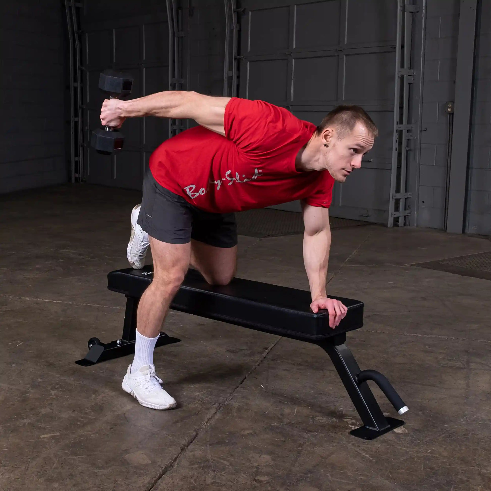 A person performing a dumbbell exercise on the Body-Solid Pro Clubline Flat Bench SFB125 in a gym setting.