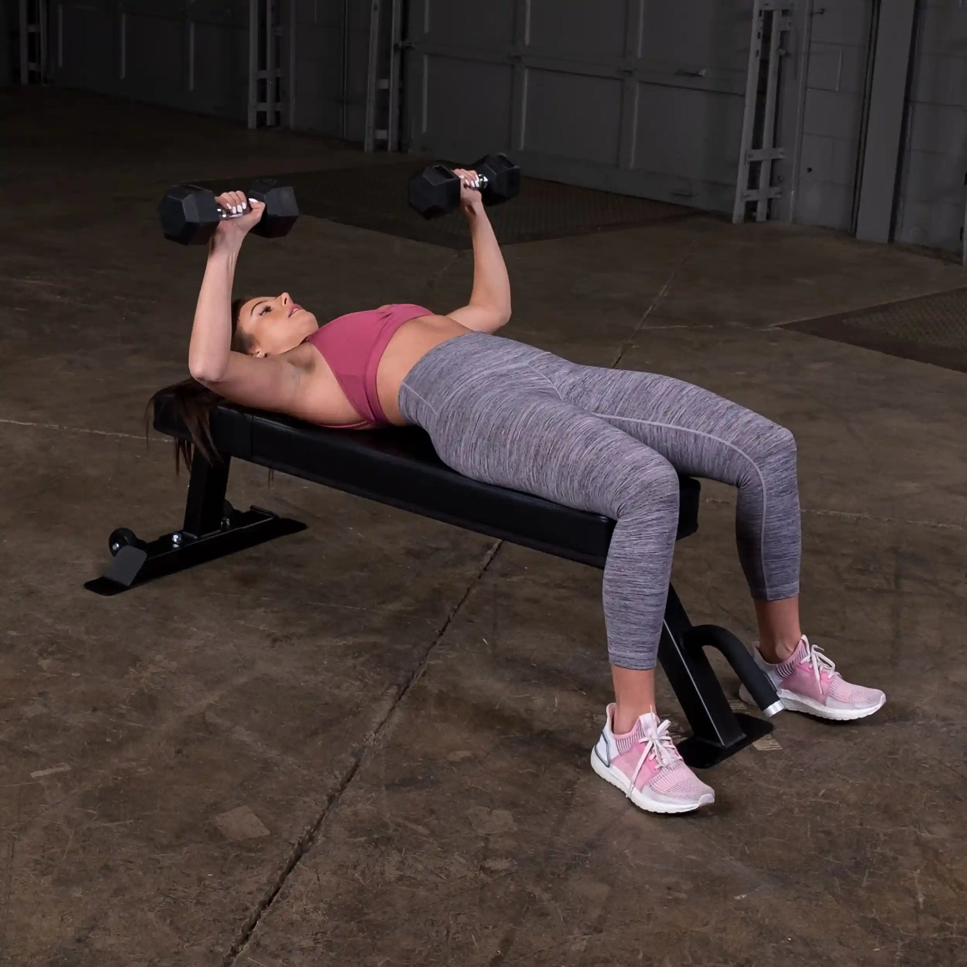 A woman performing a chest press exercise with dumbbells while lying on a Body-Solid Pro Clubline Flat Bench SFB125.