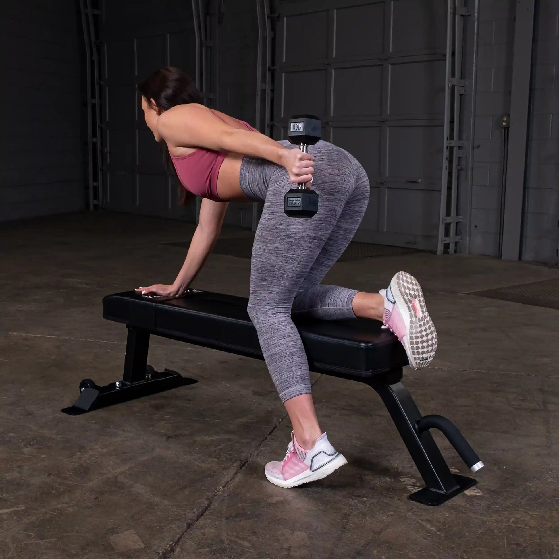 A woman performing an exercise with a dumbbell on the Body-Solid Pro Clubline Flat Bench SFB125 in a gym setting.