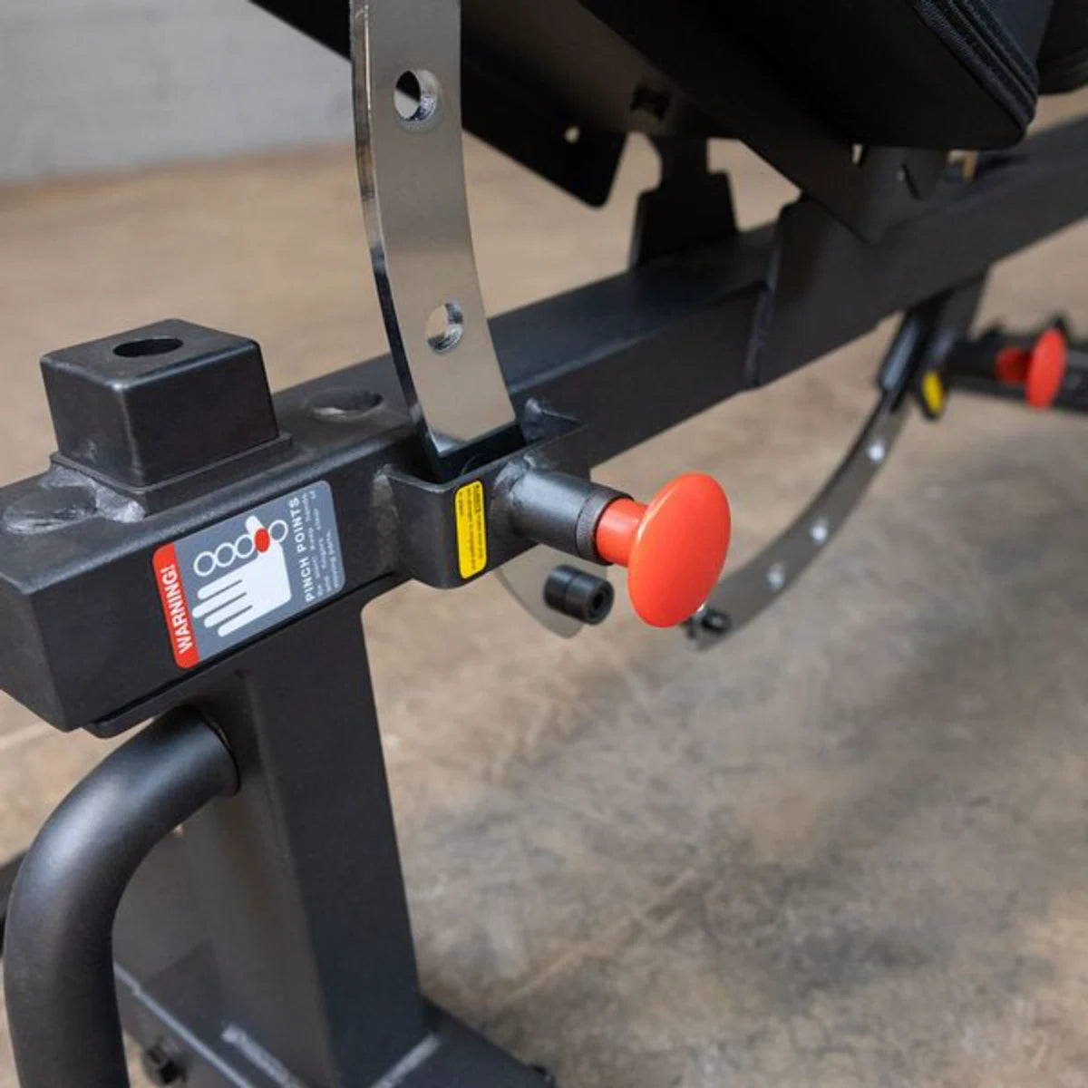 Close-up view of the adjustment mechanism and safety features on the Body-Solid Pro Clubline Flat/Incline Bench SFI20, highlighting the red release button and warning labels.