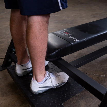 Close-up of a person's feet on a platform next to the Body-Solid Pro Clubline Flat Olympic Bench SOFB250, showcasing the bench's design and sturdy construction.