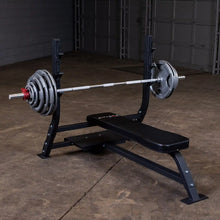 Image of the Body-Solid Pro Clubline Flat Olympic Bench SOFB250, featuring a barbell with weights, set up in a spacious gym environment.