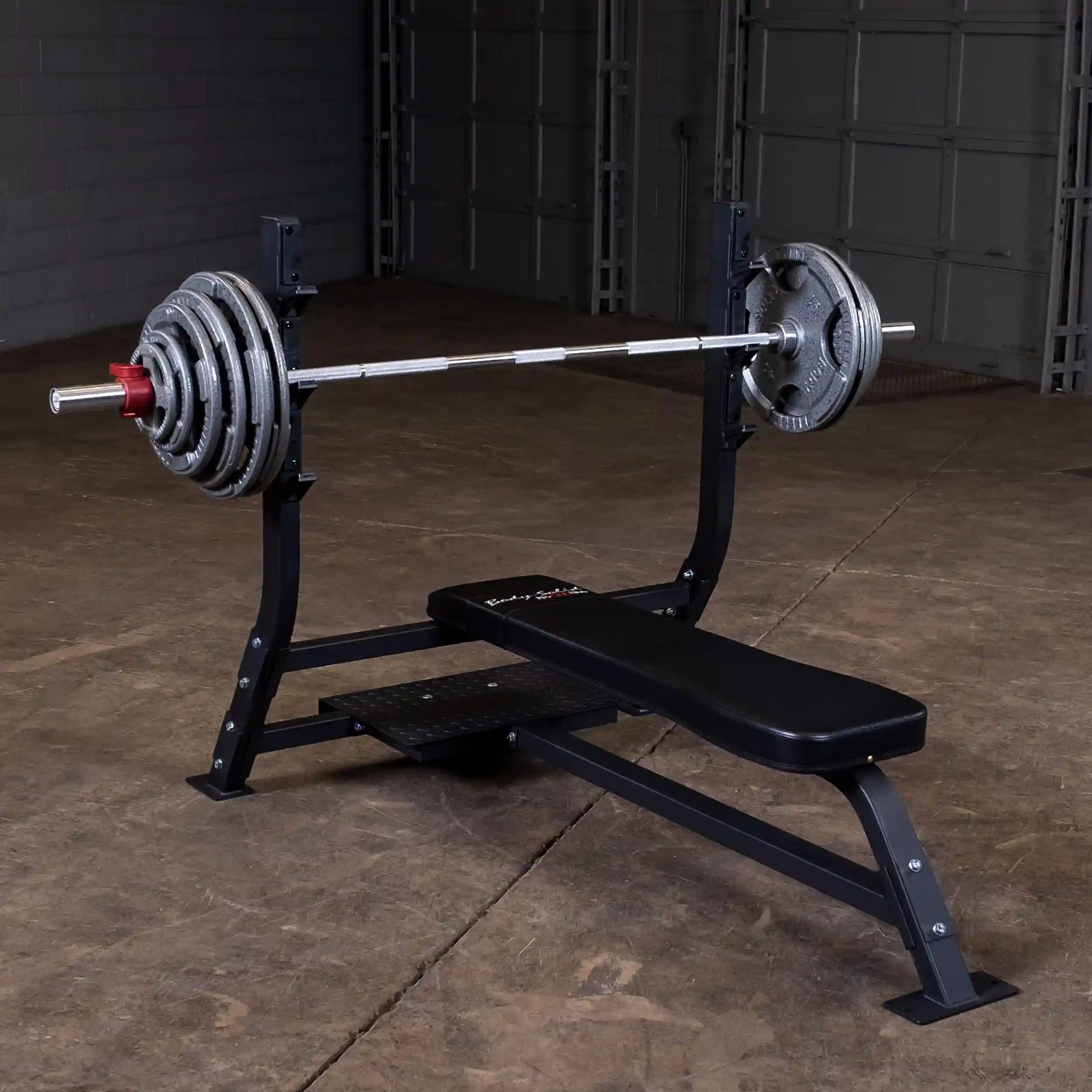 Body-Solid Pro Clubline Flat Olympic Bench SOFB250 with a barbell and weights, set in a gym environment with a concrete floor.
