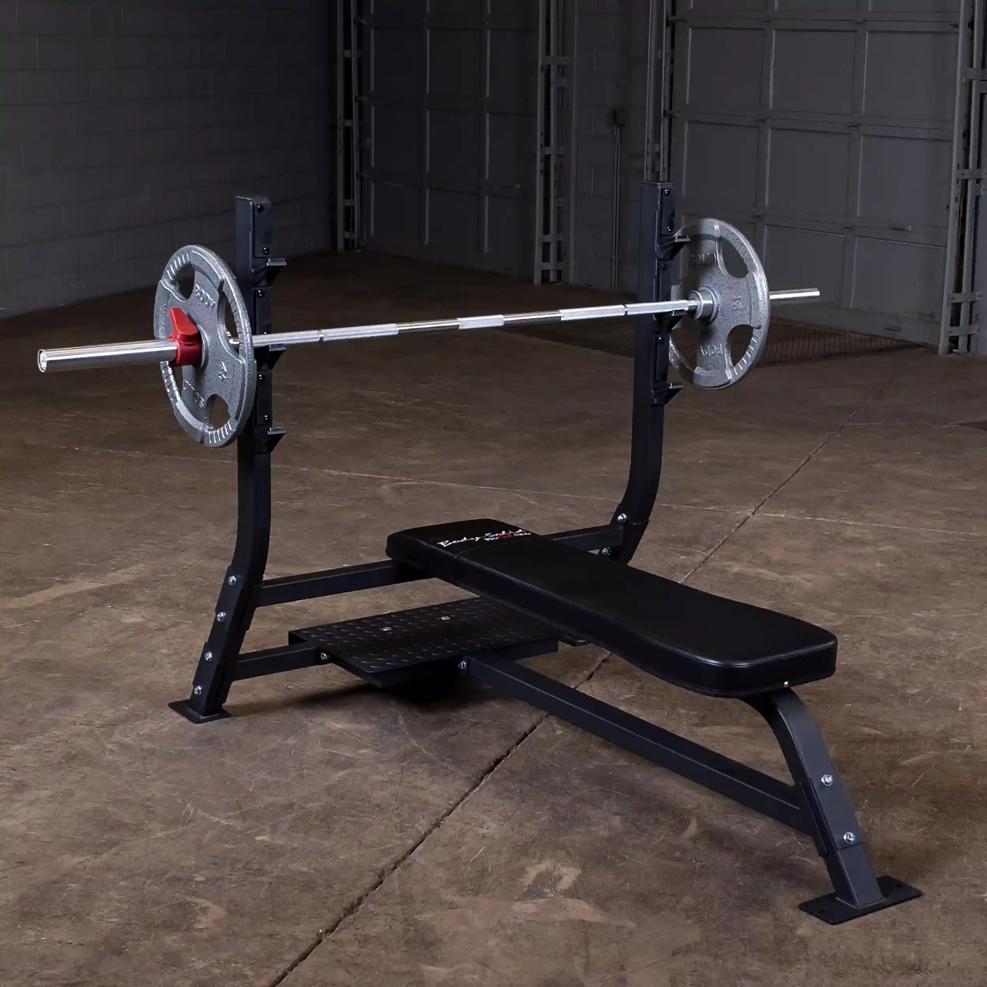 Body-Solid Pro Clubline Flat Olympic Bench SOFB250 with a barbell and weight plates, set up in a gym space with a concrete floor.