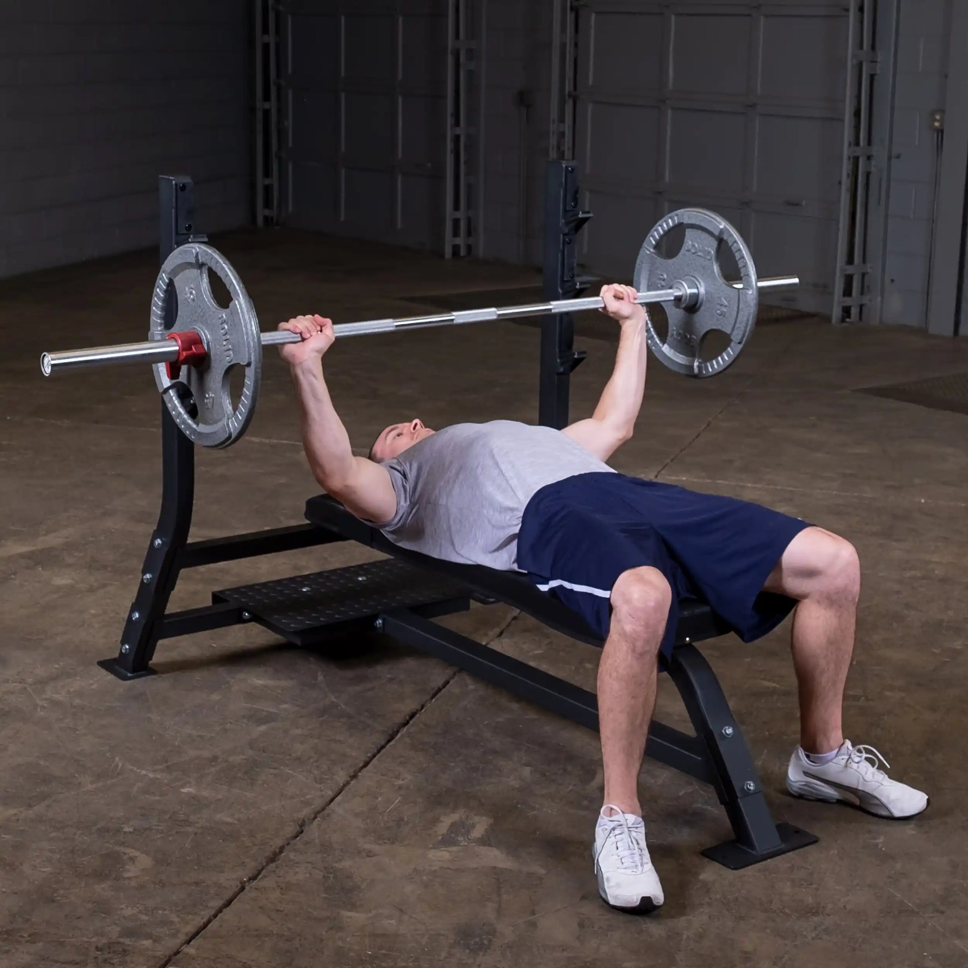 A man performing a bench press exercise on the Body-Solid Pro Clubline Flat Olympic Bench SOFB250 in a gym setting.