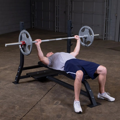 A man performing a bench press exercise on the Body-Solid Pro Clubline Flat Olympic Bench SOFB250 in a gym setting.