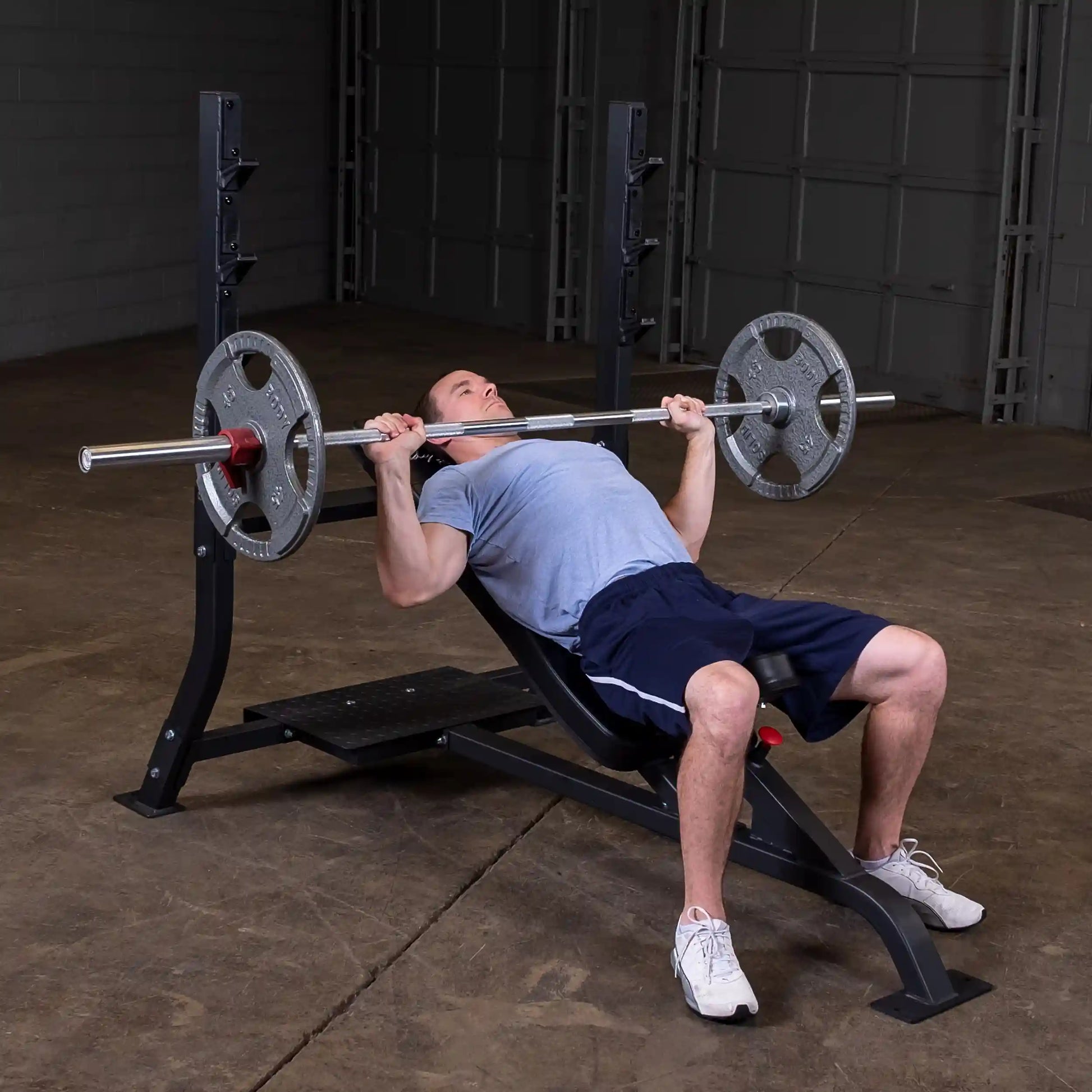 A person performing an incline bench press on the Body-Solid Pro Clubline Incline Olympic Bench SOIB250, with a barbell and weight plates, in a gym setting.