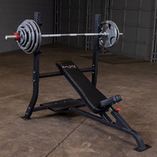 Image of a Body-Solid Pro Clubline Incline Olympic Bench SOIB250 with a barbell and weight plates, set up on a concrete floor in a gym environment.