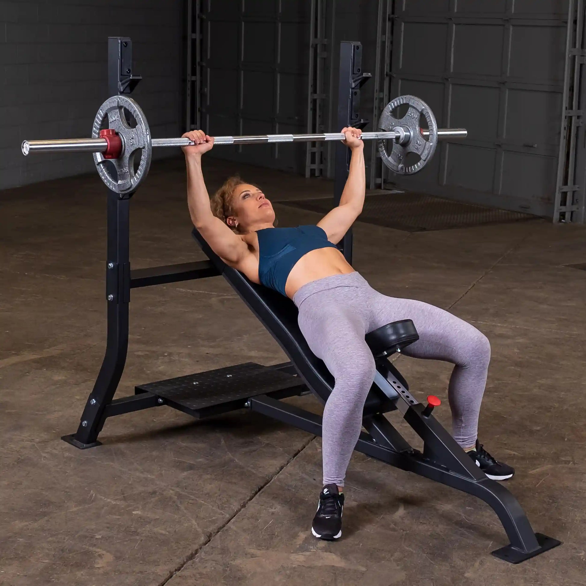 A person performing a bench press on the Body-Solid Pro Clubline Incline Olympic Bench SOIB250, with a barbell and weights, in a gym setting.