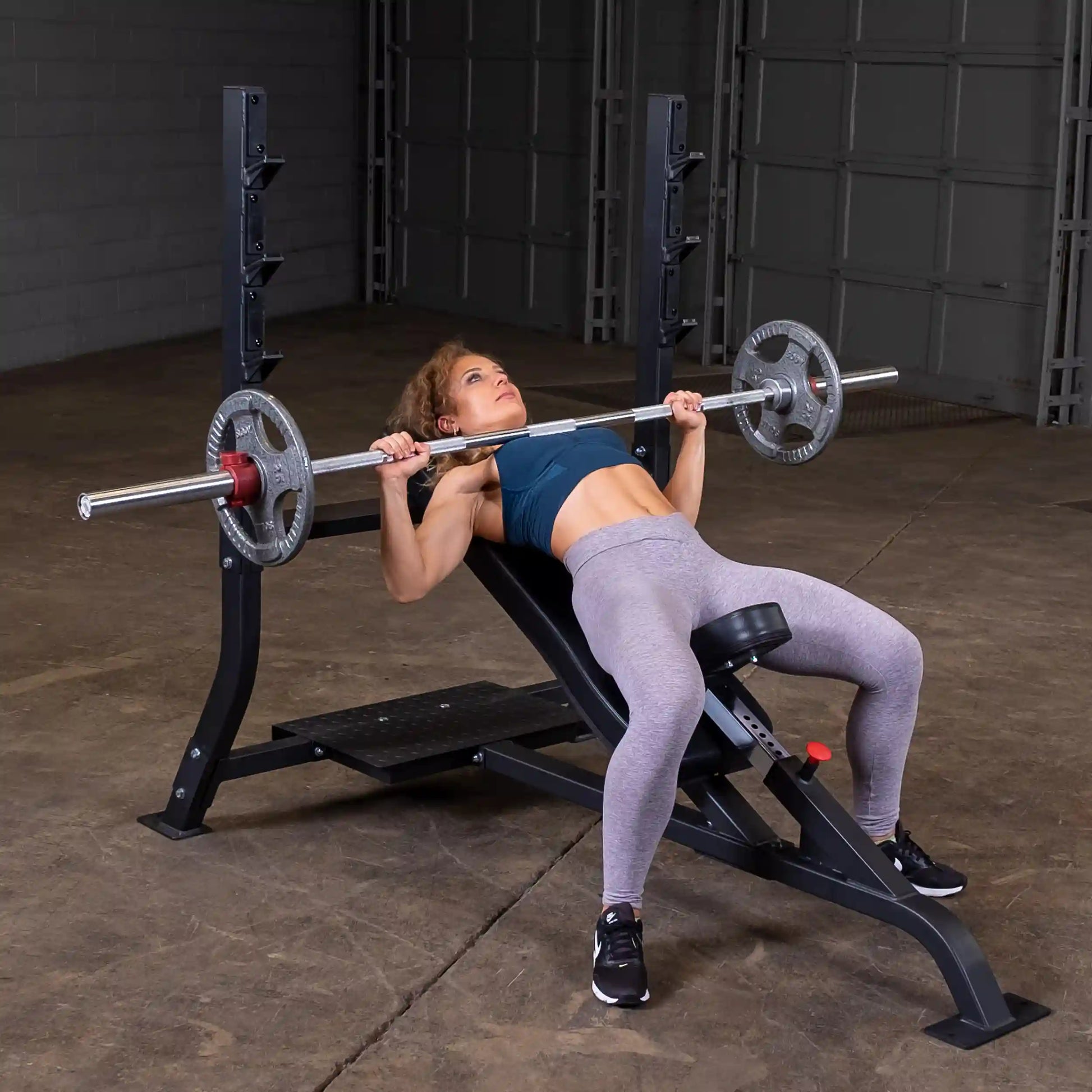 A woman performs an incline bench press on the Body-Solid Pro Clubline Incline Olympic Bench SOIB250, with a barbell and weights, in a gym setting.