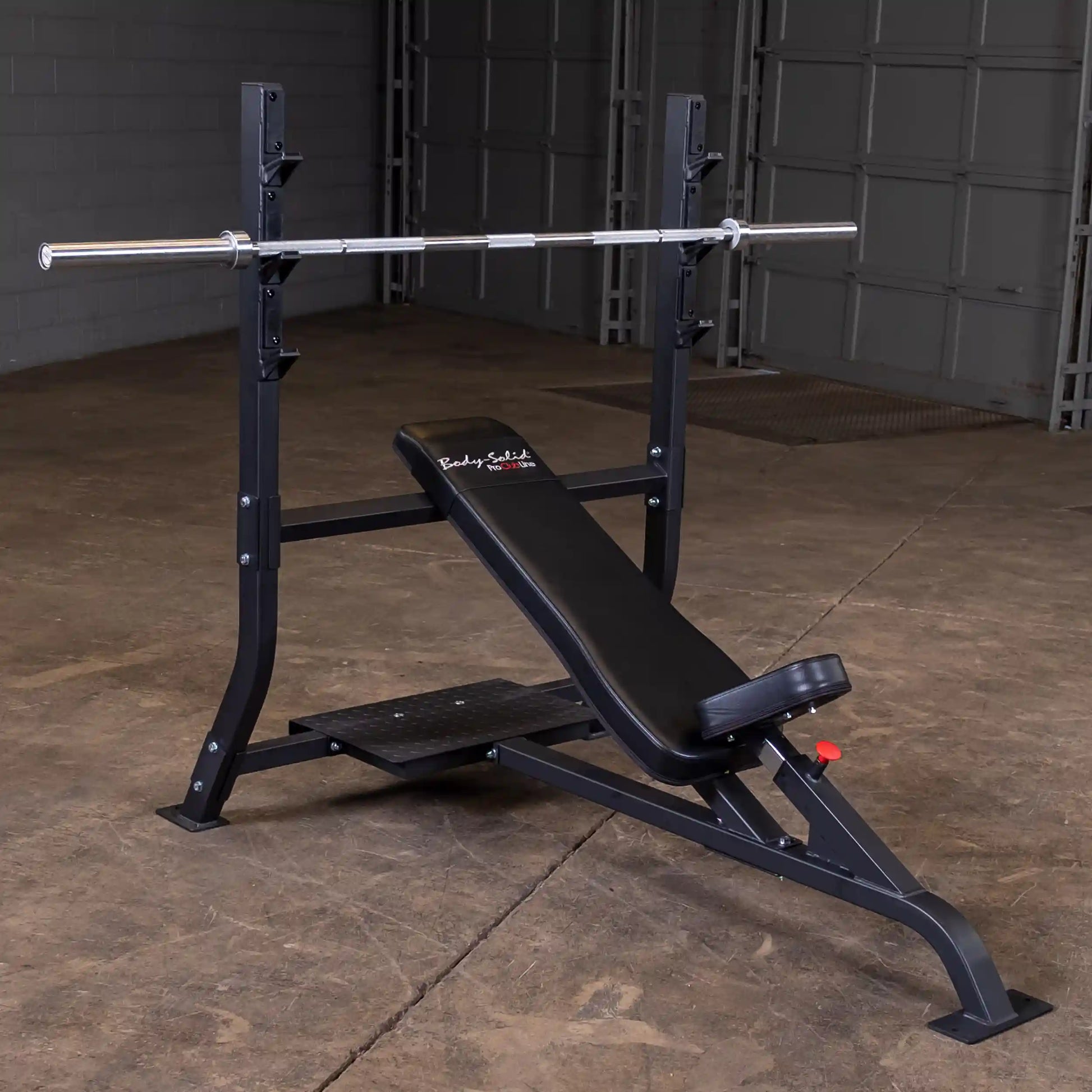 Body-Solid Pro Clubline Incline Olympic Bench SOIB250, featuring a sturdy black frame, adjustable incline seat, and a barbell rack, positioned on a concrete floor in a spacious gym setting.