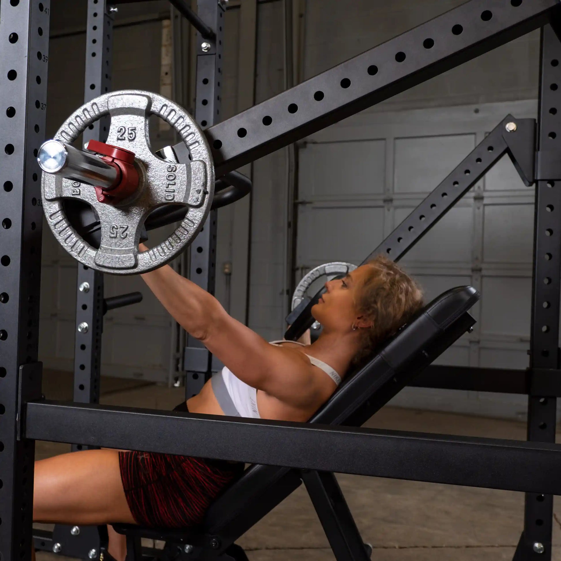 A person exercising on an incline bench with Body-Solid Pro Clubline Jammer Arms SPRJAM, lifting weights in a gym setting.
