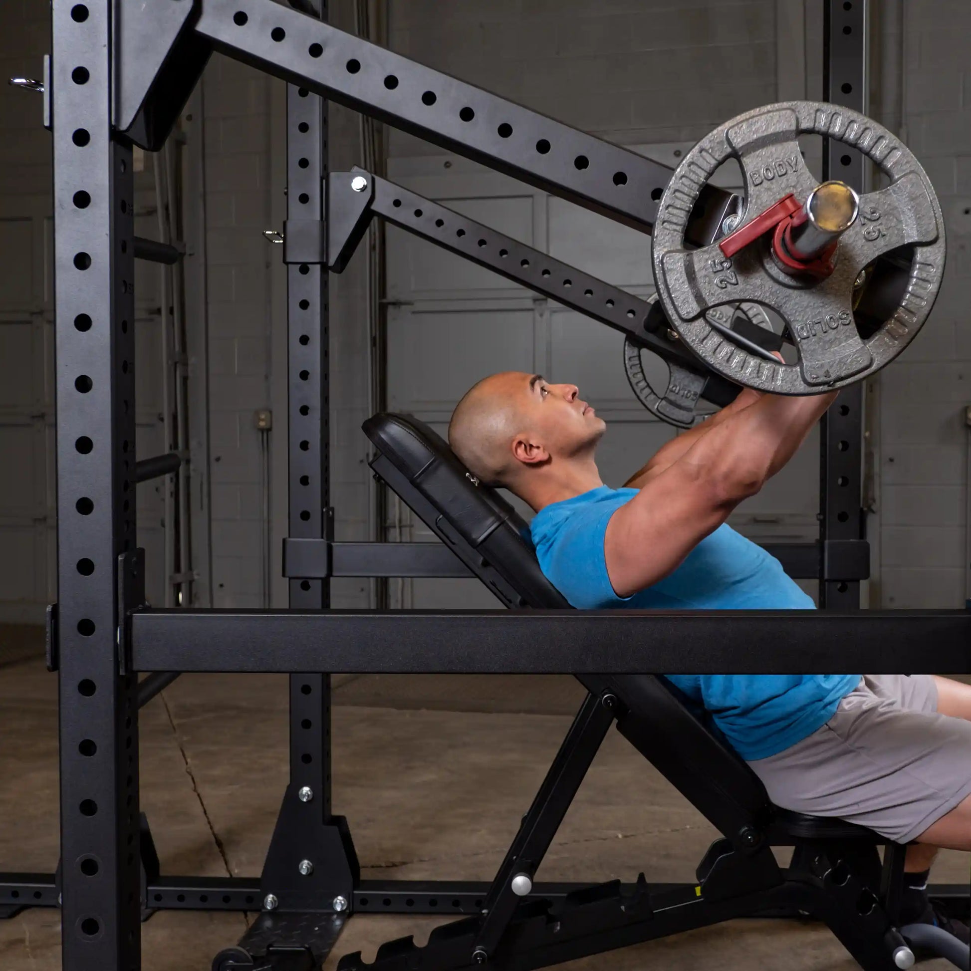 A person performing an exercise using the Body-Solid Pro Clubline Jammer Arms SPRJAM, lying on a bench and pressing a weight overhead in a gym setting.
