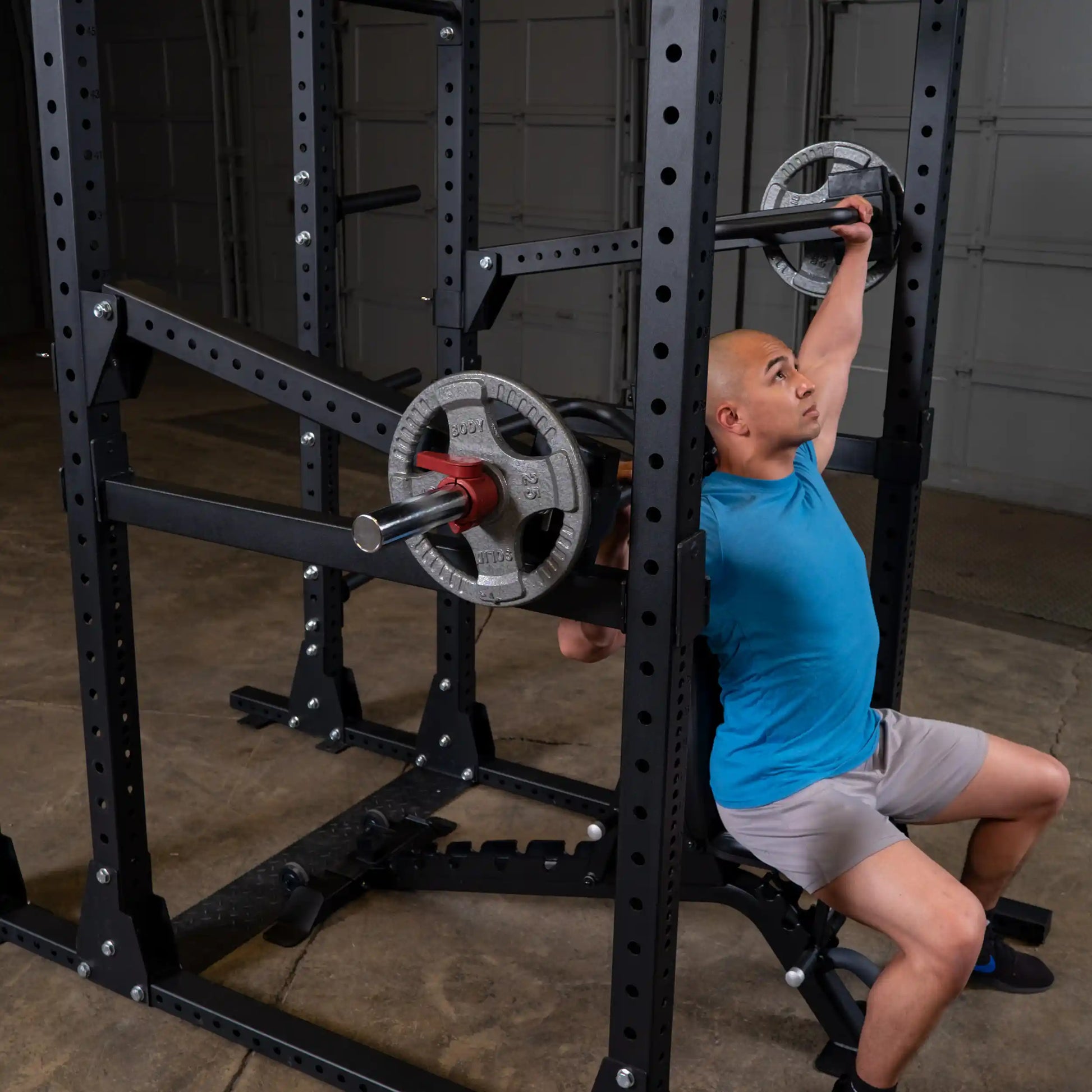 A person performing an exercise using the Body-Solid Pro Clubline Jammer Arms SPRJAM, seated and pressing weights overhead in a gym setting.