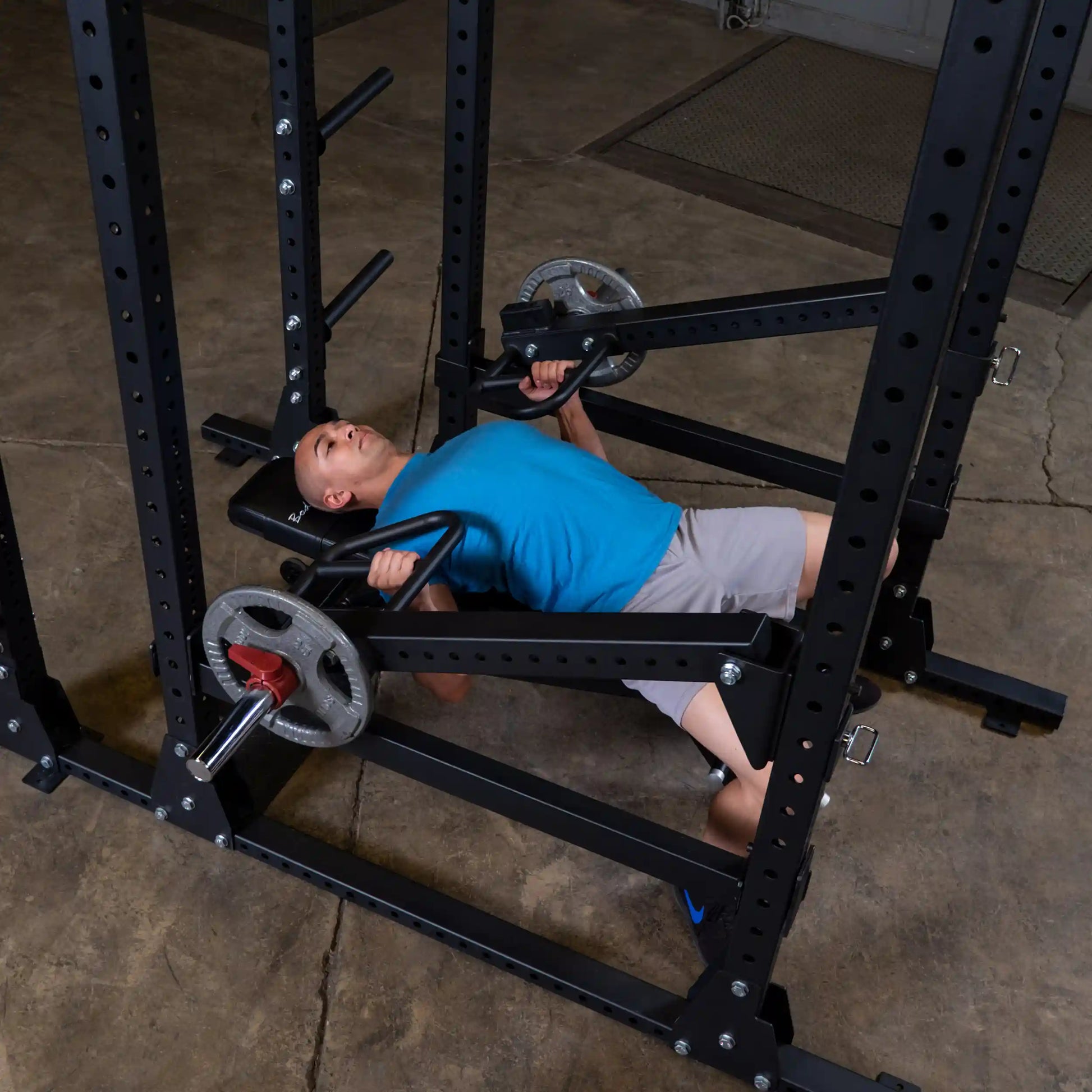 A person performing a bench press exercise using the Body-Solid Pro Clubline Jammer Arms SPRJAM attached to a squat rack.