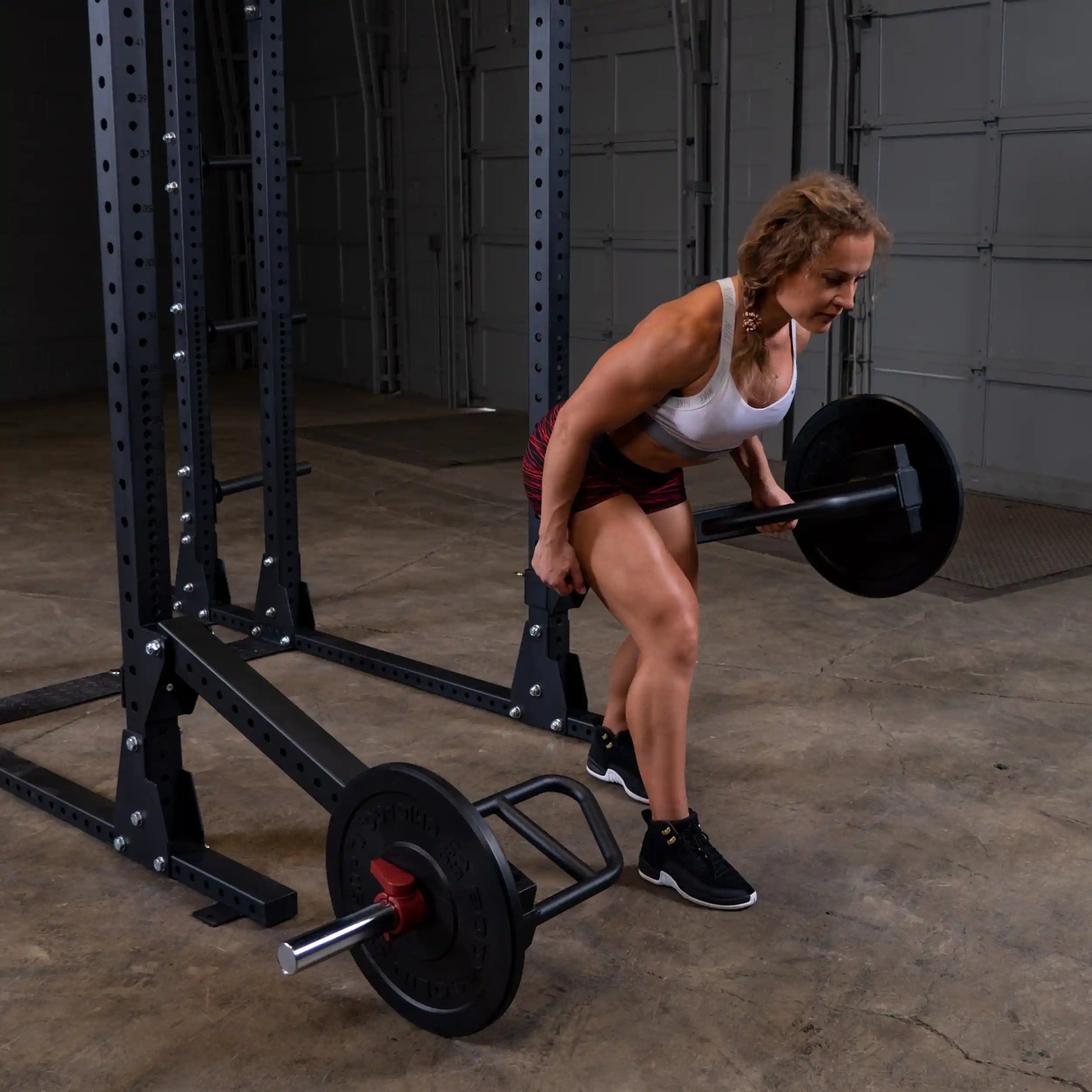 A person performing an exercise using the Body-Solid Pro Clubline Jammer Arms SPRJAM in a gym setting, focusing on strength training with a barbell.