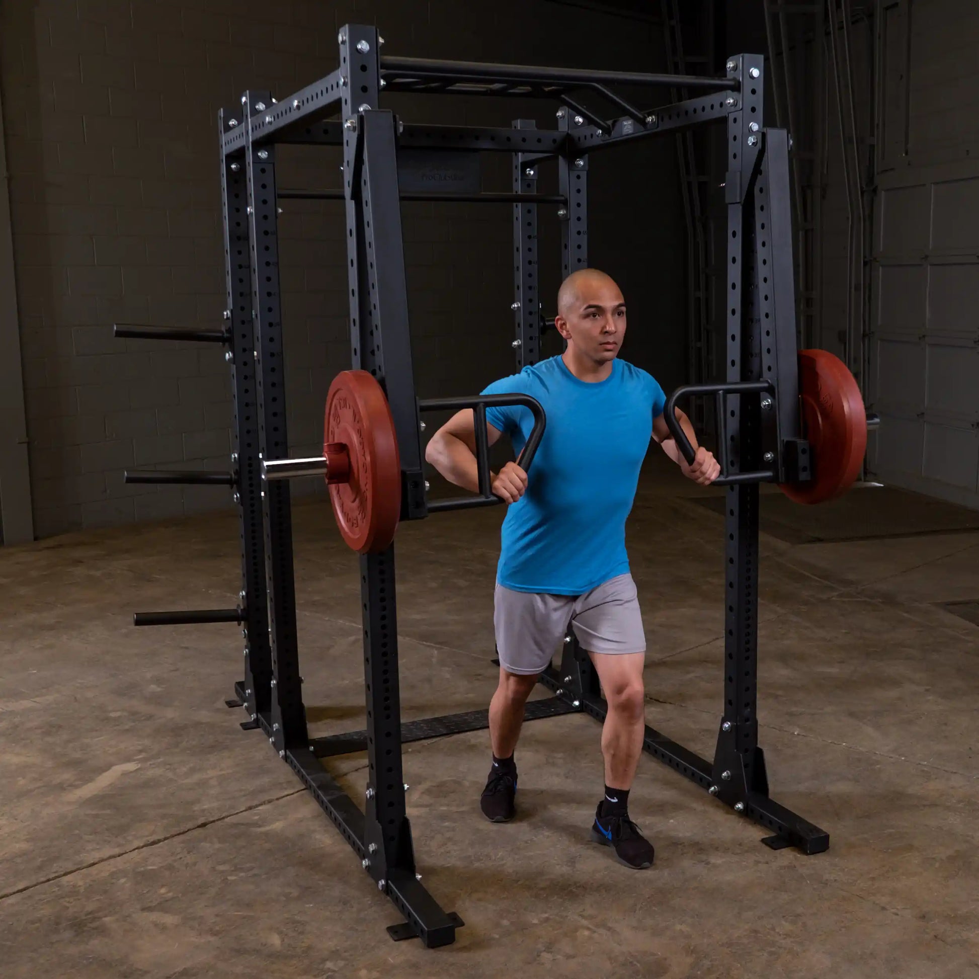 Person performing a squat exercise using the Body-Solid Pro Clubline Jammer Arms SPRJAM in a gym setting, showcasing the equipment's functionality.
