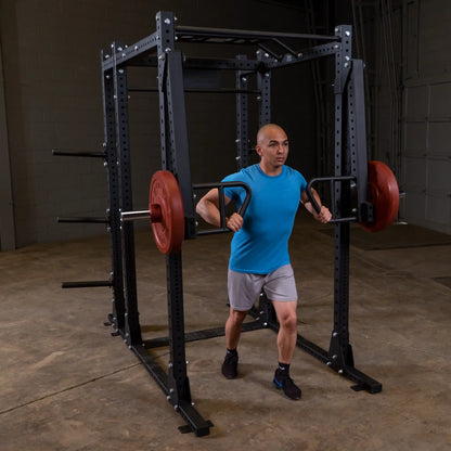 Person performing a squat exercise using the Body-Solid Pro Clubline Jammer Arms SPRJAM in a gym setting, showcasing the equipment's functionality.