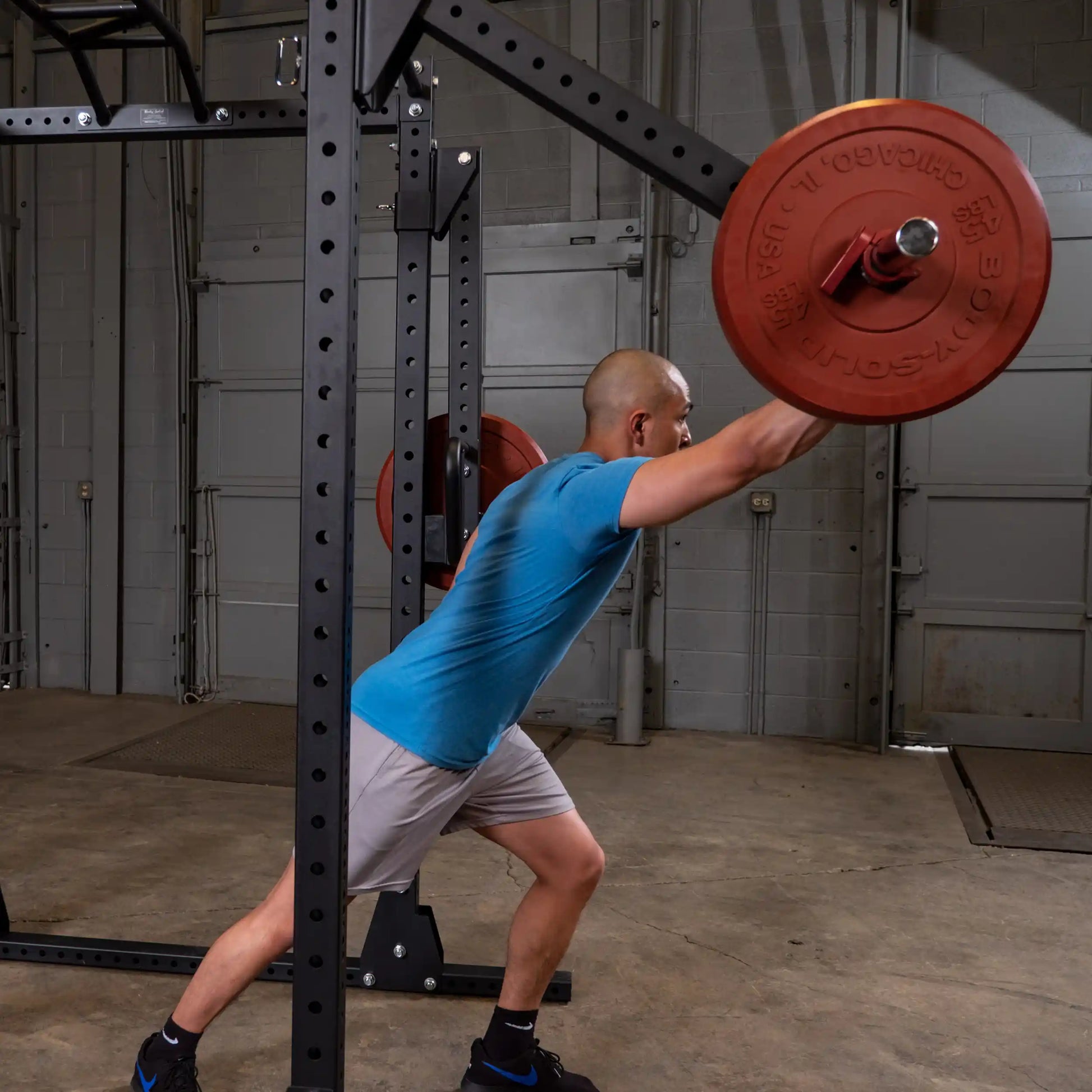 A person performing an exercise with the Body-Solid Pro Clubline Jammer Arms SPRJAM, pushing a barbell overhead in a gym setting.