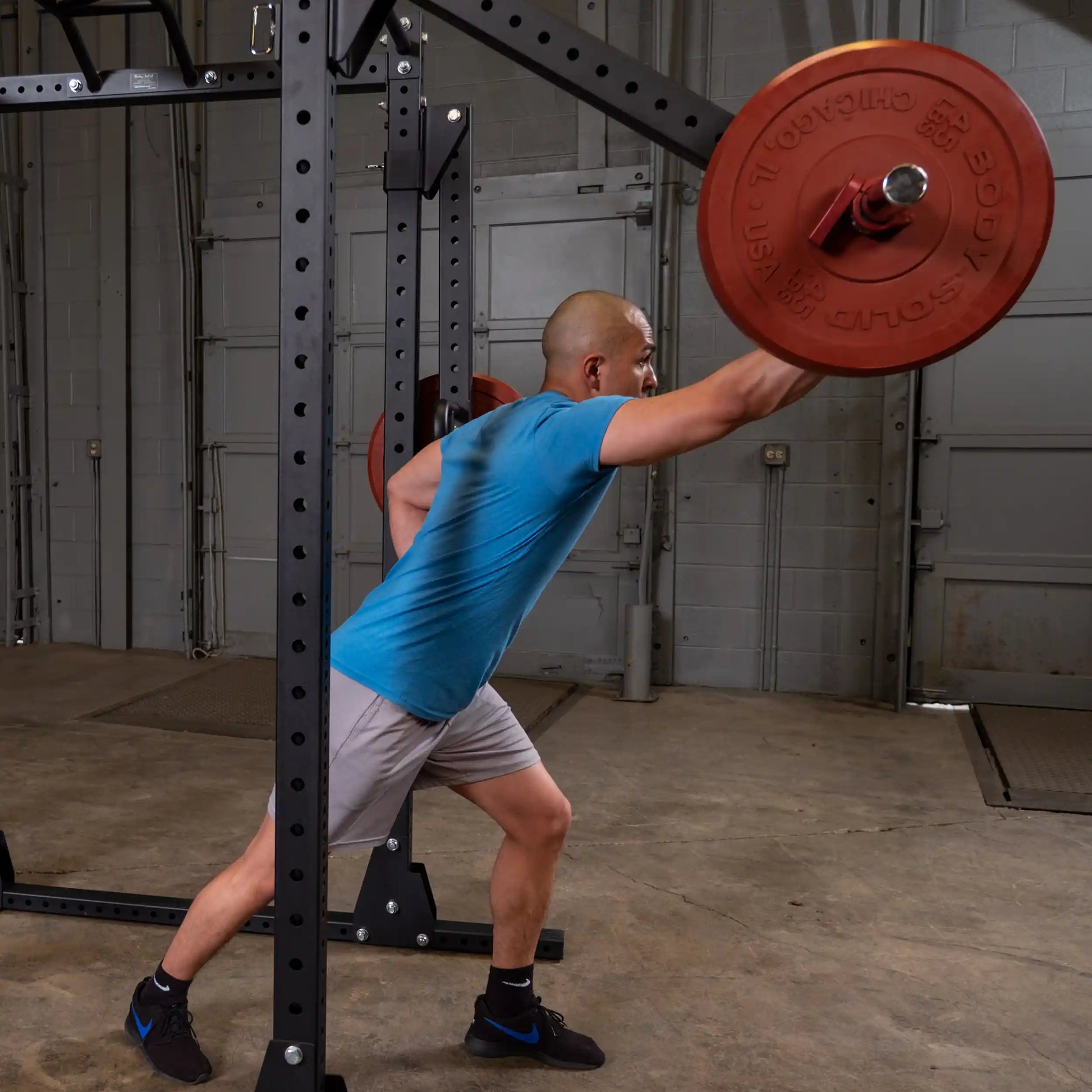A person executing an exercise using the Body-Solid Pro Clubline Jammer Arms SPRJAM in a gym setting, with a barbell loaded with weights.
