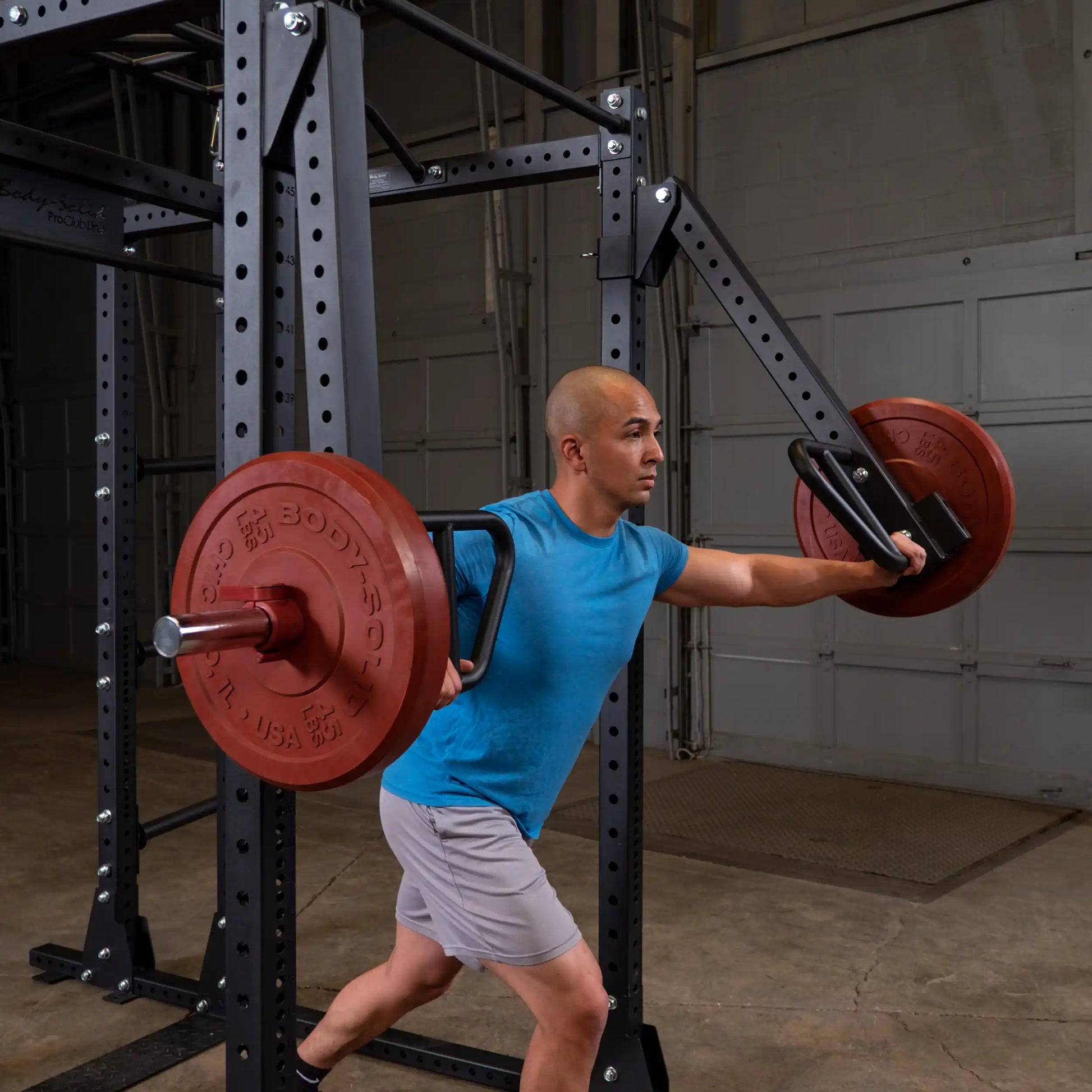 A person performing an exercise with the Body-Solid Pro Clubline Jammer Arms SPRJAM, showcasing a weightlifting setup in a gym environment.