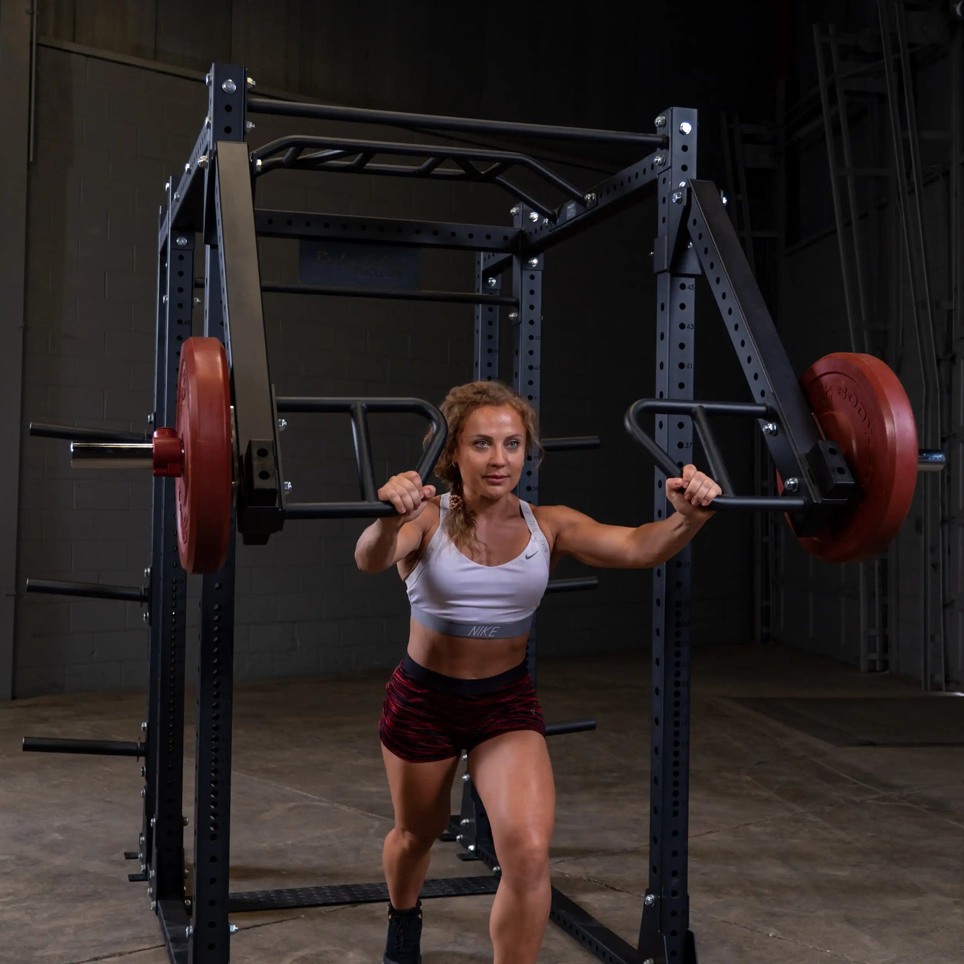 A woman performing an exercise using the Body-Solid Pro Clubline Jammer Arms SPRJAM, showcasing strength training in a gym setting with weights on the apparatus.