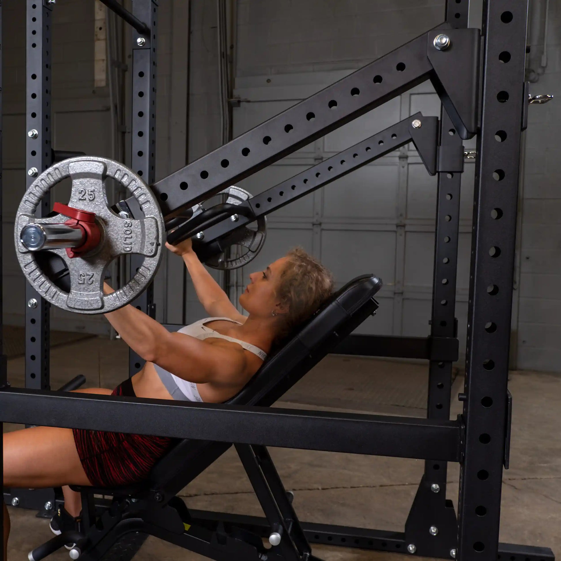 A woman exercising on a Body-Solid Pro Clubline Jammer Arms SPRJAM machine, performing an incline press with weights in a gym setting.
