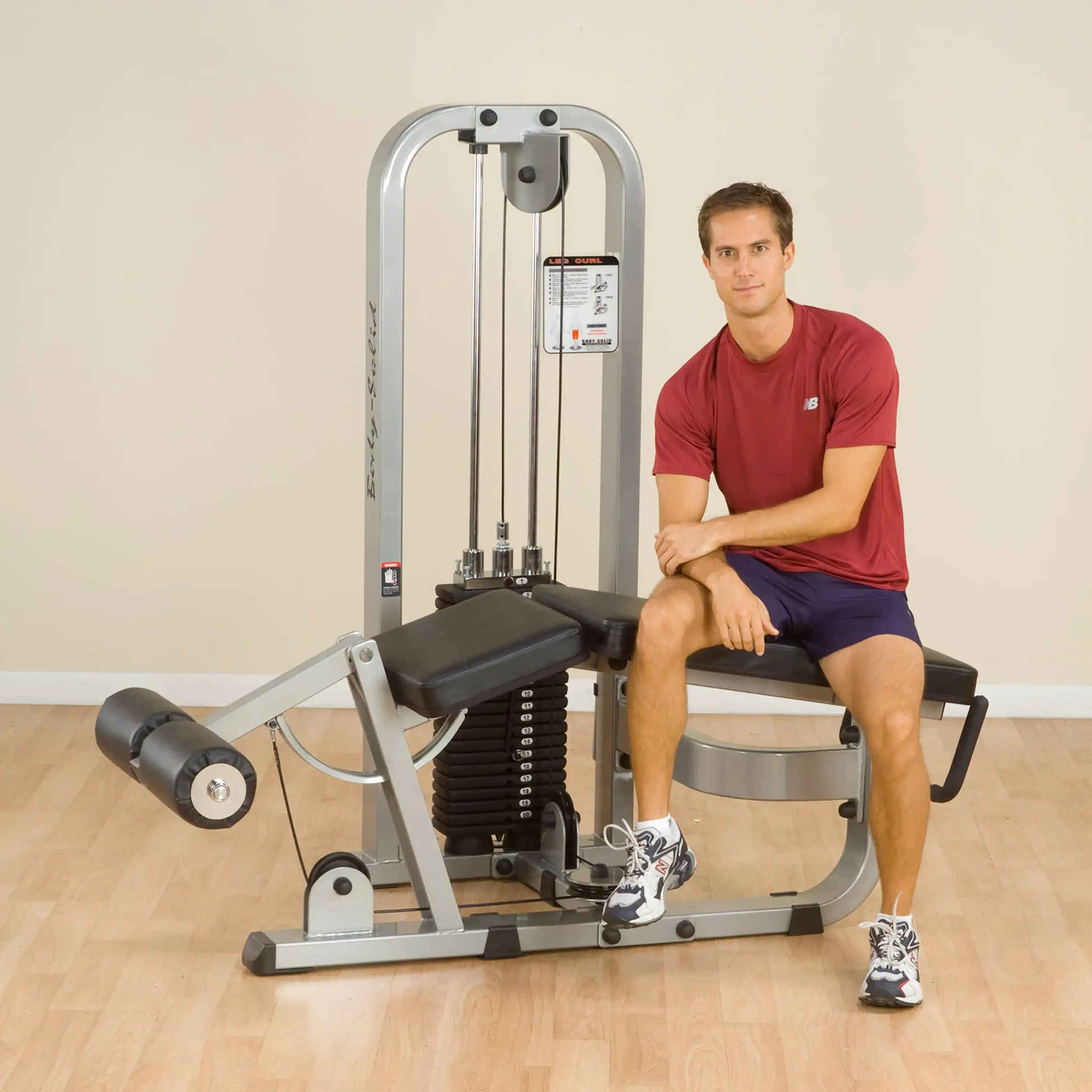 A man sitting on the Body-Solid Pro Clubline Leg Curl Machine SLC400G, demonstrating the equipment in a fitness setting.