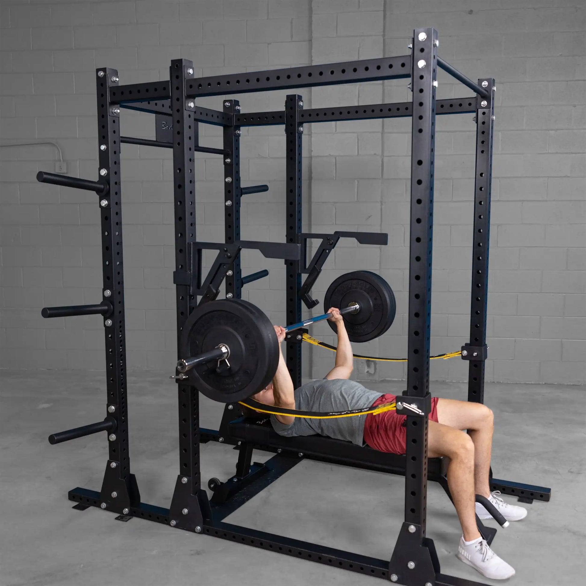 A person using the Body-Solid Pro Clubline Monolift Attachment SPRLFT to perform a bench press inside a gym, equipped with a squat rack and weights.