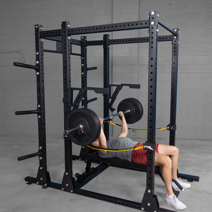 A person using the Body-Solid Pro Clubline Monolift Attachment SPRLFT to perform a bench press inside a gym, equipped with a squat rack and weights.