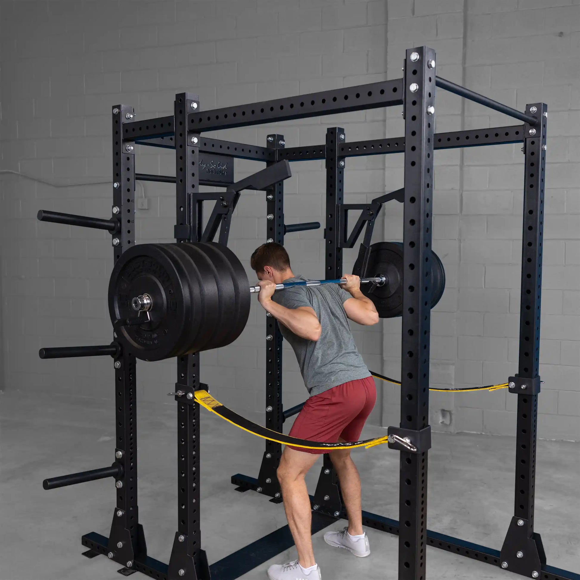 A person performing a squat using the Body-Solid Pro Clubline Monolift Attachment SPRLFT, featuring a weightlifting setup with a barbell and weights within a gym environment.