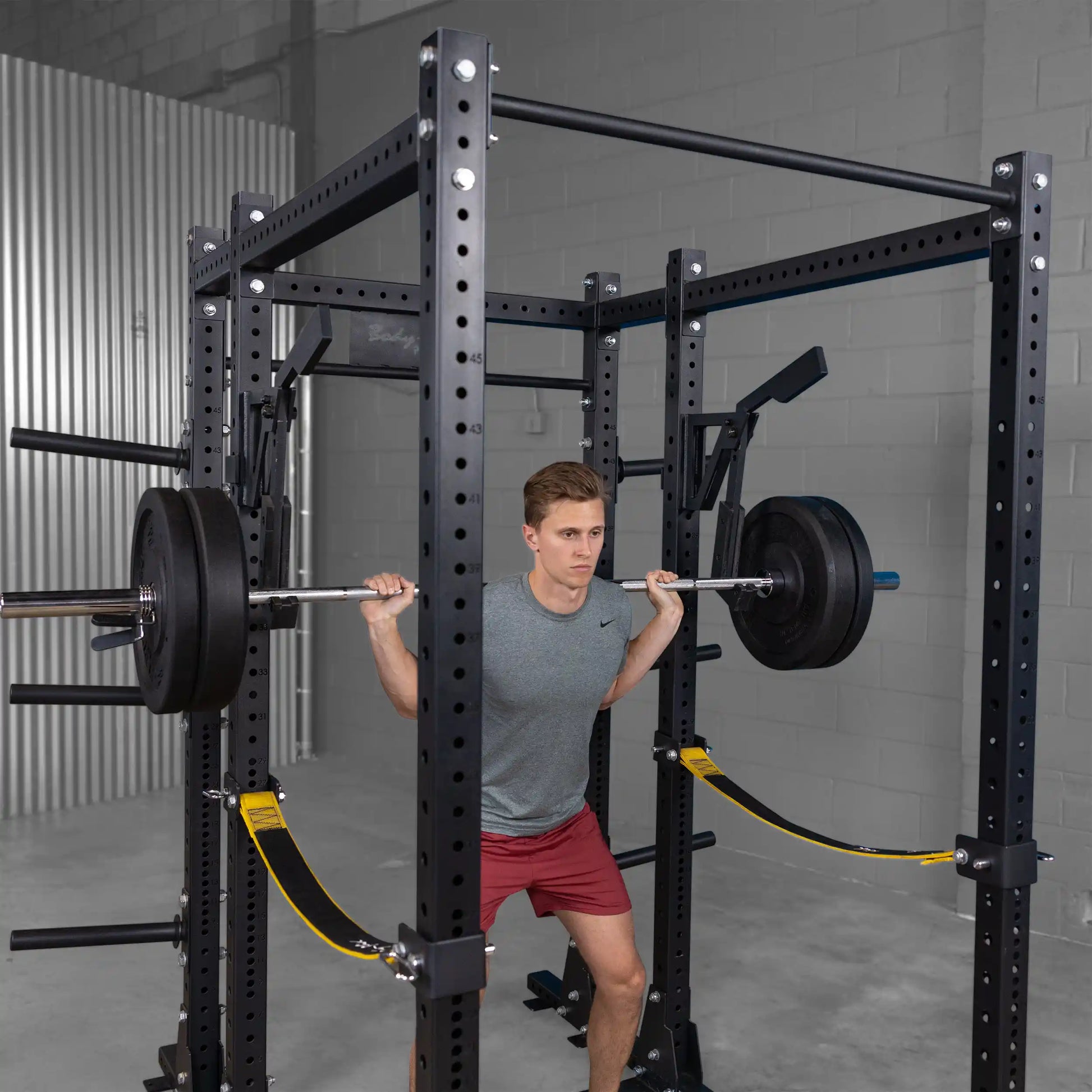 Person performing a squat with a barbell in a gym setting, utilizing the Body-Solid Pro Clubline Monolift Attachment SPRLFT, demonstrating strength training.