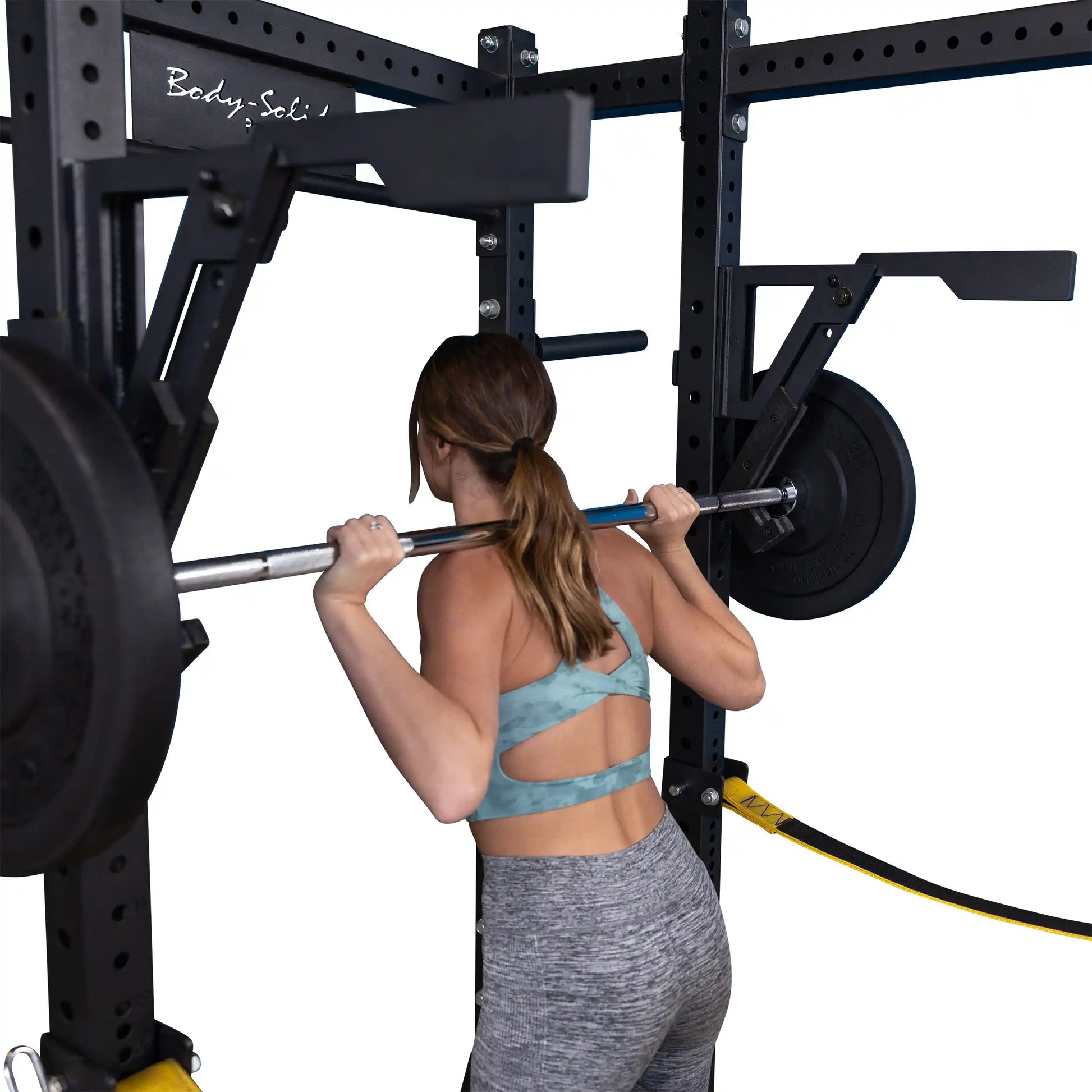 A person performing a squat with a barbell using the Body-Solid Pro Clubline Monolift Attachment SPRLFT, showcasing the equipment in a gym setting.