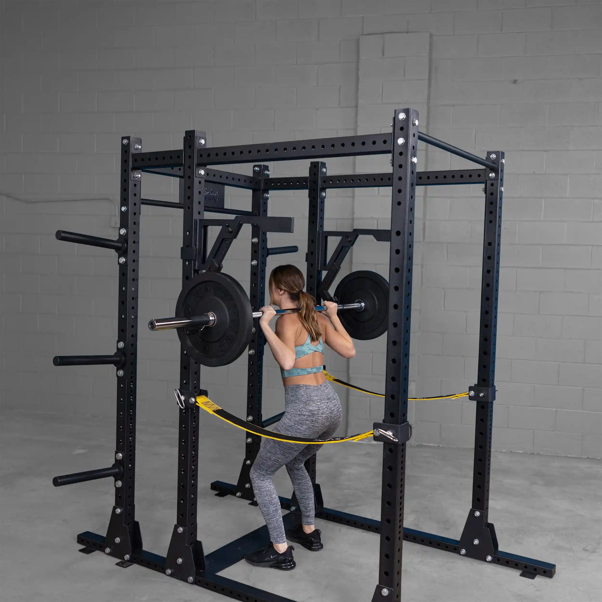 A woman performs squats using the Body-Solid Pro Clubline Monolift Attachment SPRLFT, with weights on the barbell inside a gym setting.