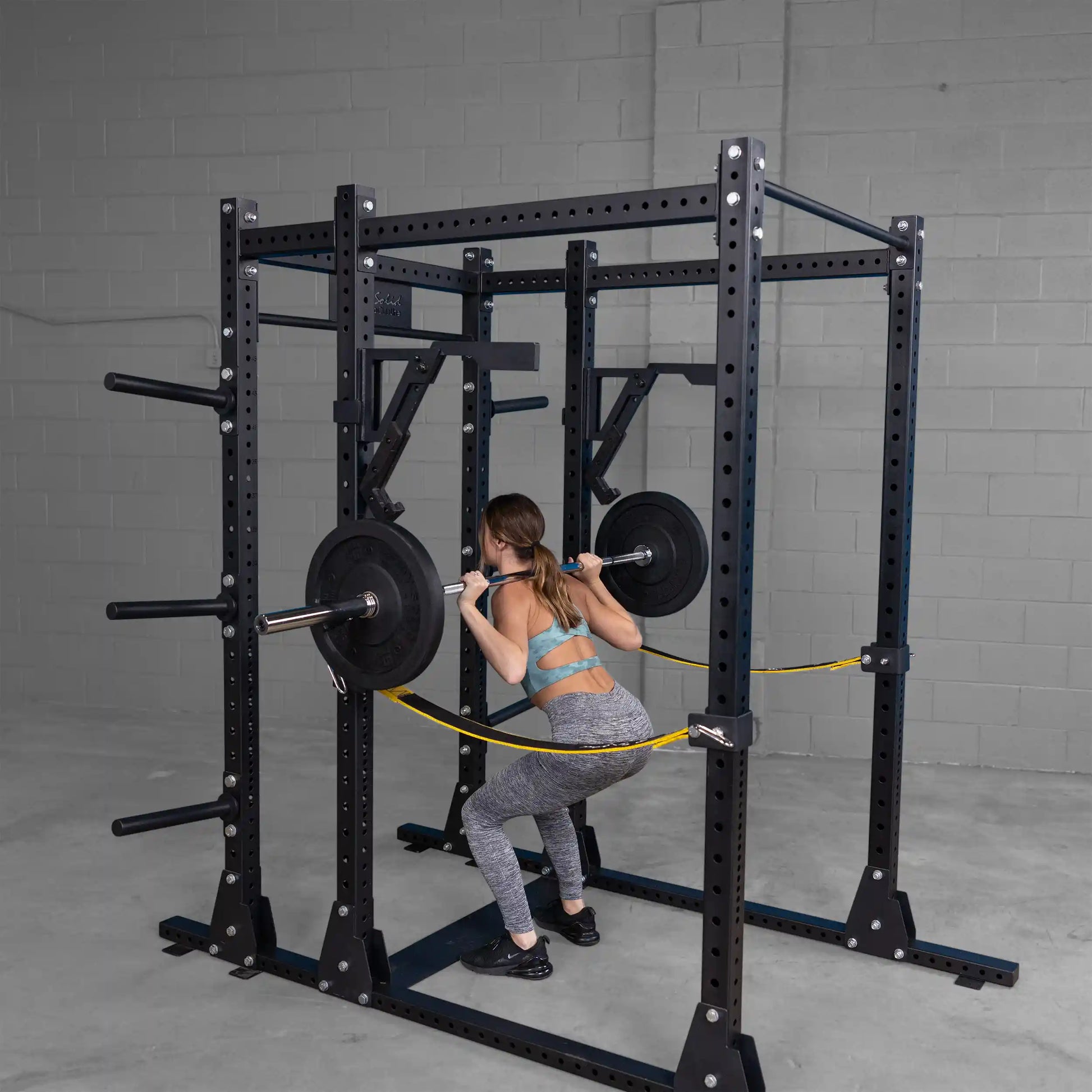 Woman performing squats using the Body-Solid Pro Clubline Monolift Attachment SPRLFT in a gym setting.