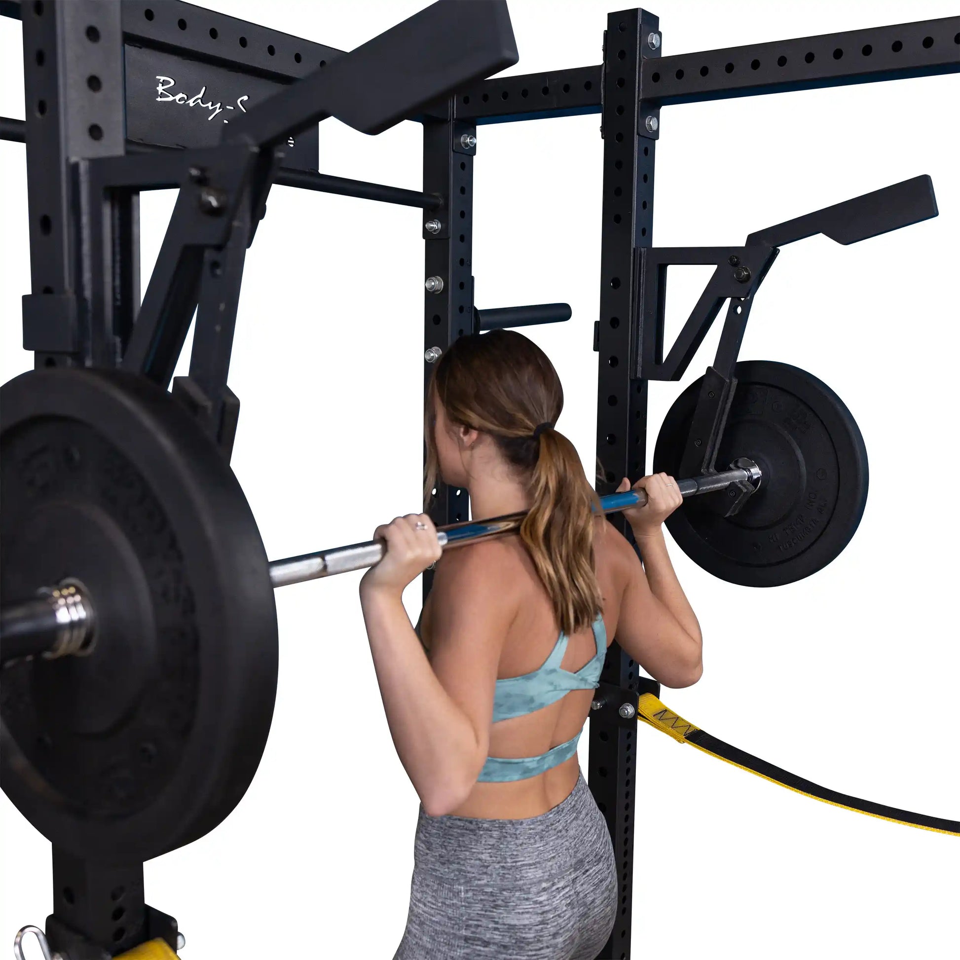 A woman performing a squat with a barbell on a Body-Solid Pro Clubline Monolift Attachment SPRLFT within a strength training setup.
