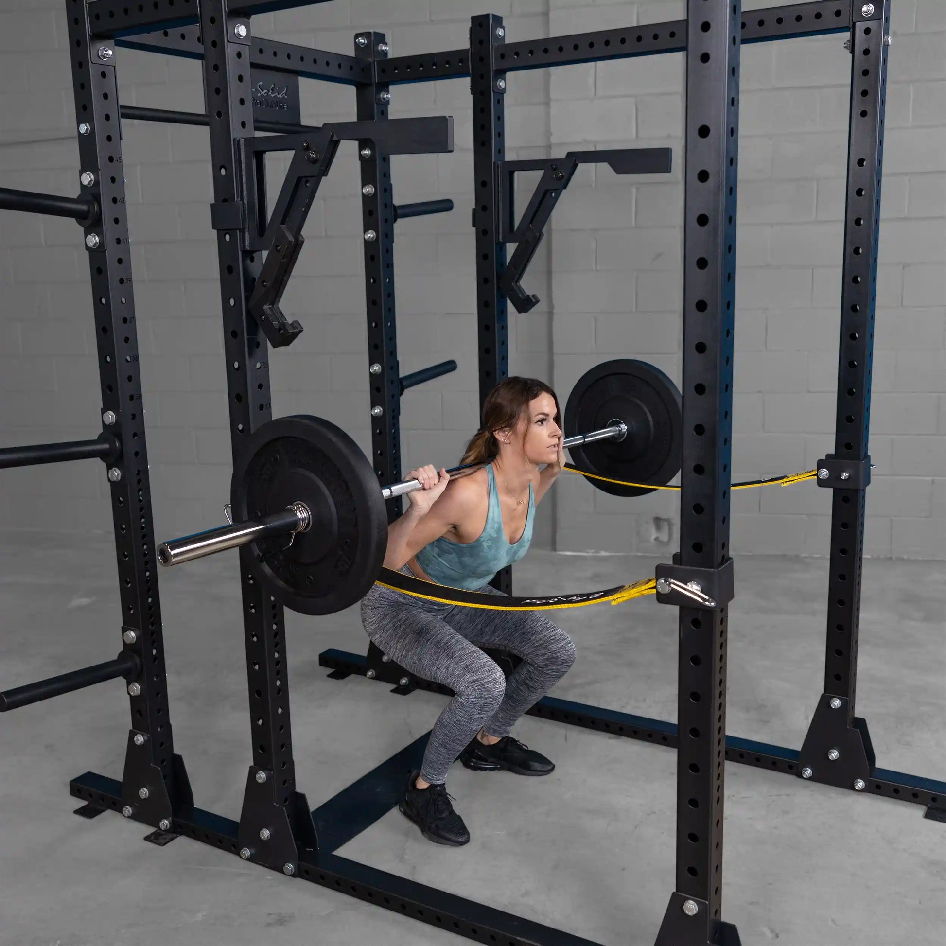Woman performing squats with a barbell using the Body-Solid Pro Clubline Monolift Attachment SPRLFT in a gym setting, showcasing the equipment's features.