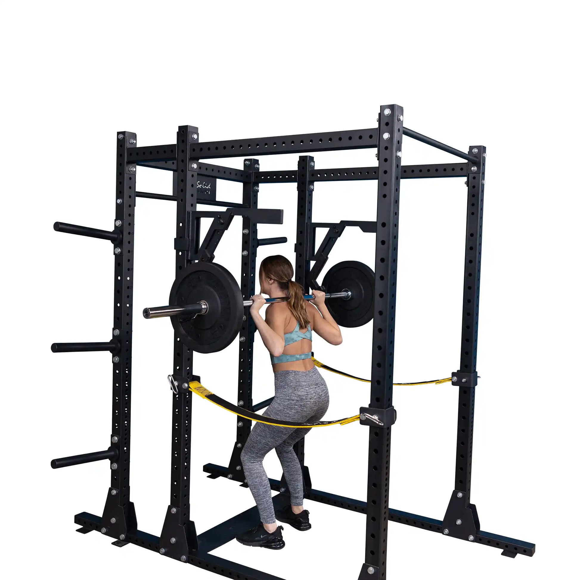 A person performing squats with the Body-Solid Pro Clubline Monolift Attachment SPRLFT, showcasing a squat rack equipped with weight plates and safety straps.