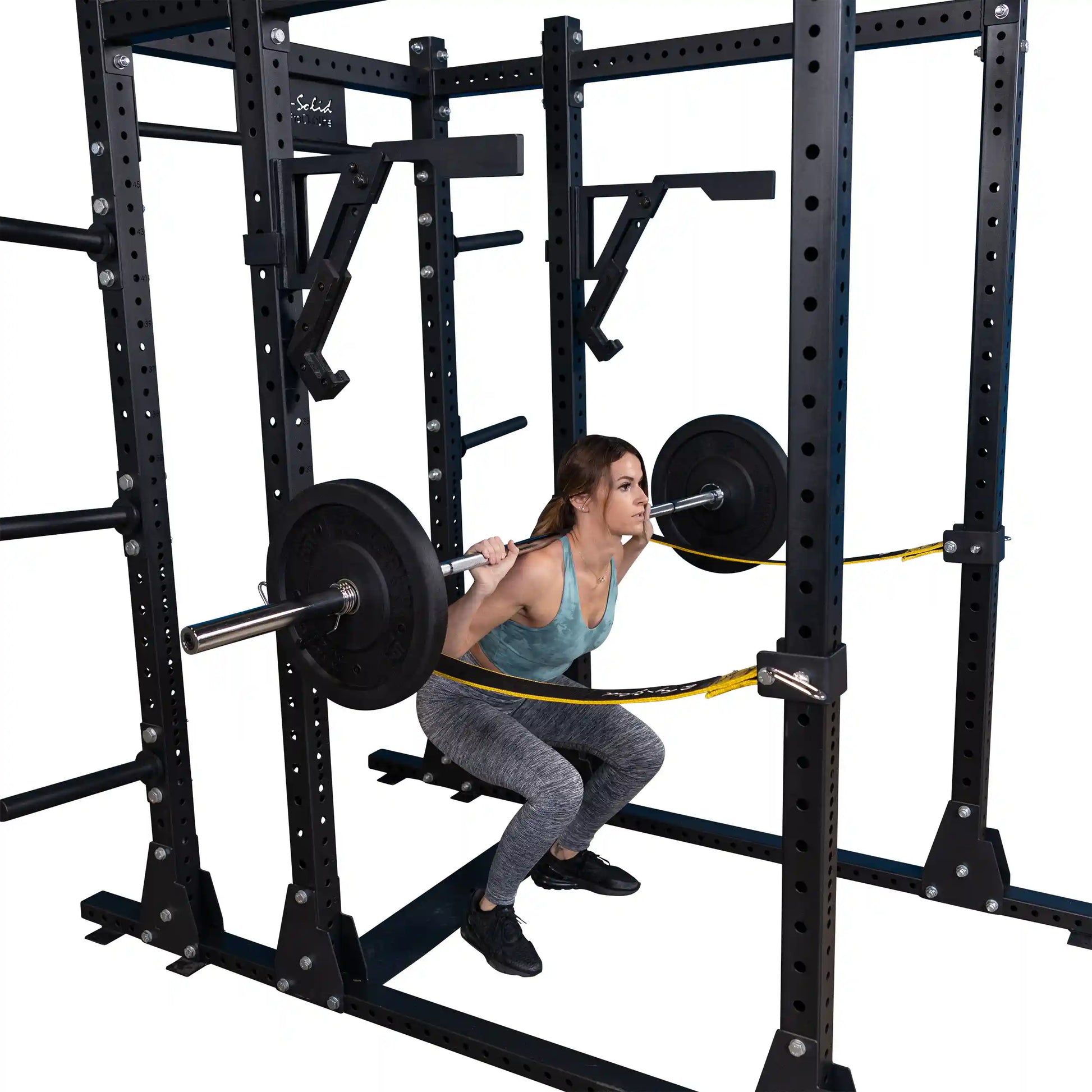A woman performing a squat with a barbell using the Body-Solid Pro Clubline Monolift Attachment SPRLFT in a gym setting.